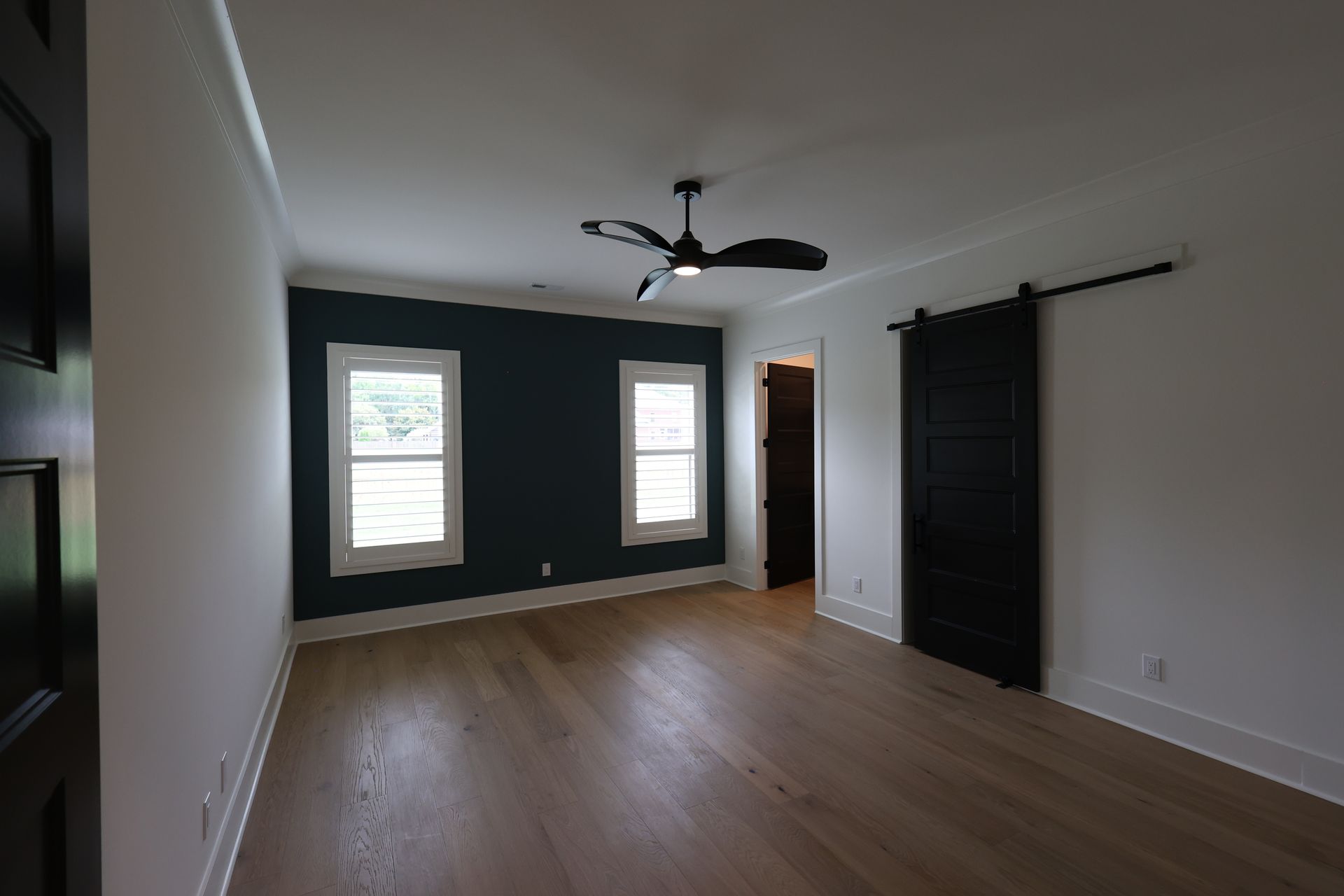 Empty bedroom with wood floors, dark accent wall, and sliding barn door.