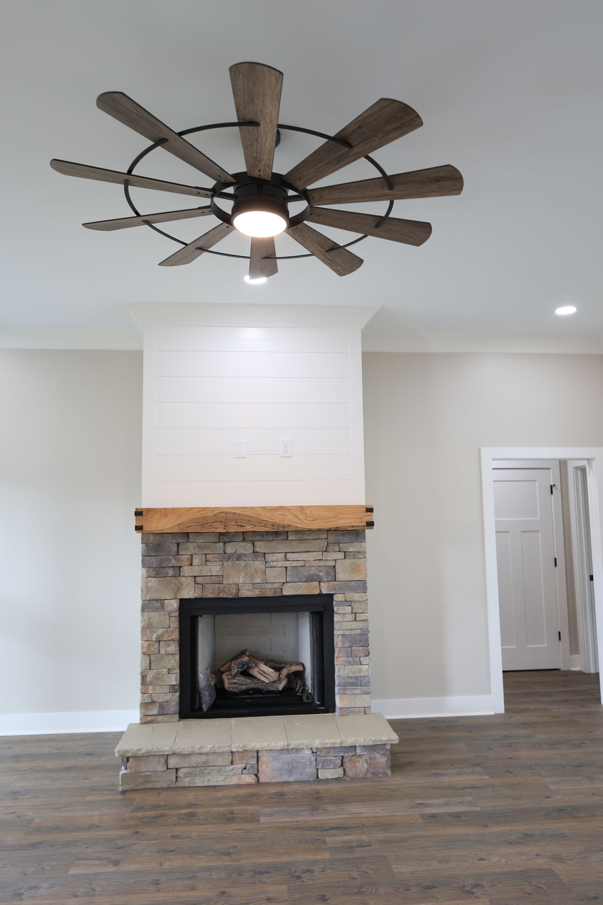 Fireplace with stone facade, wooden mantel, and rustic ceiling fan in a modern room.