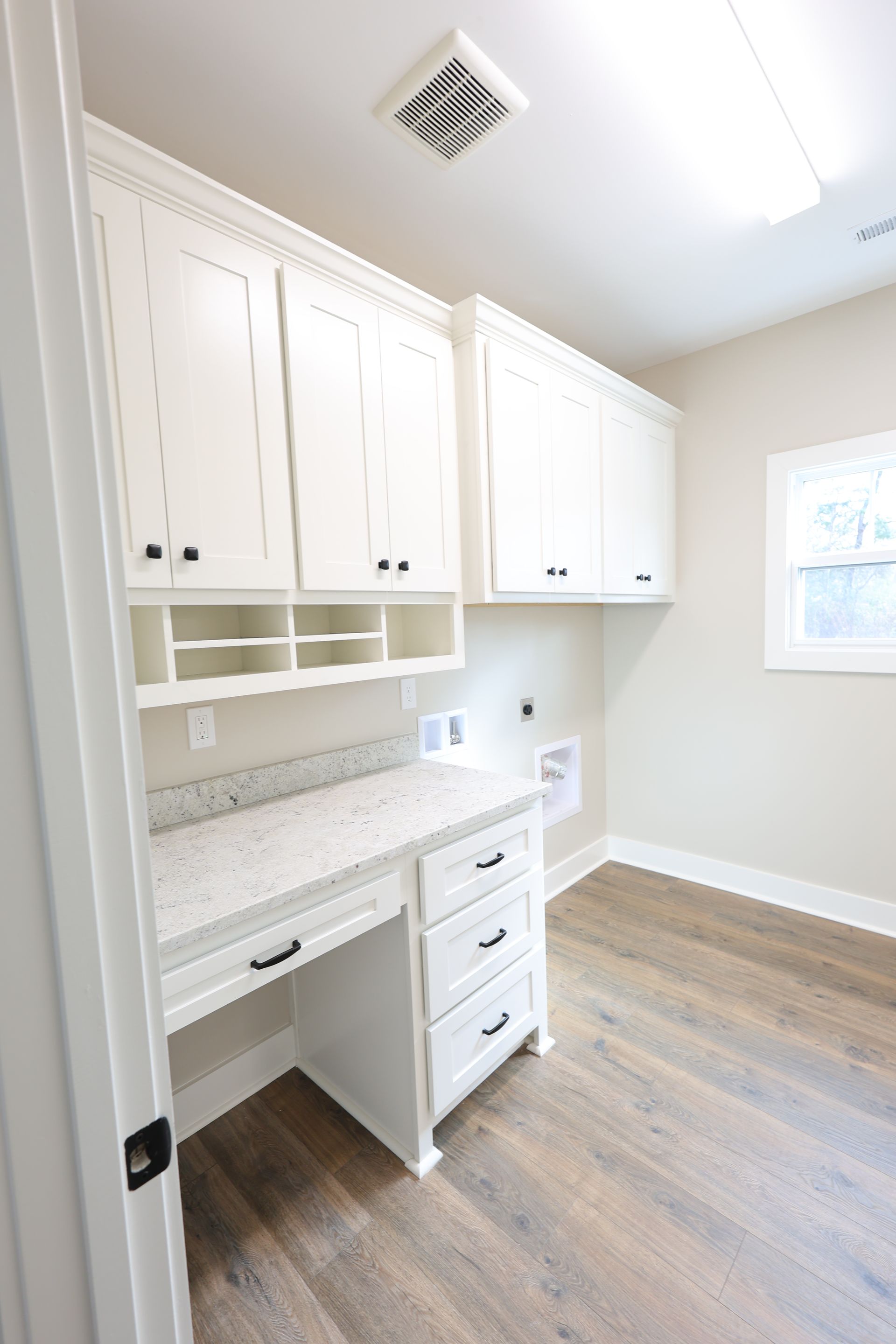 White laundry room with desk, cabinets, and hardwood floors.