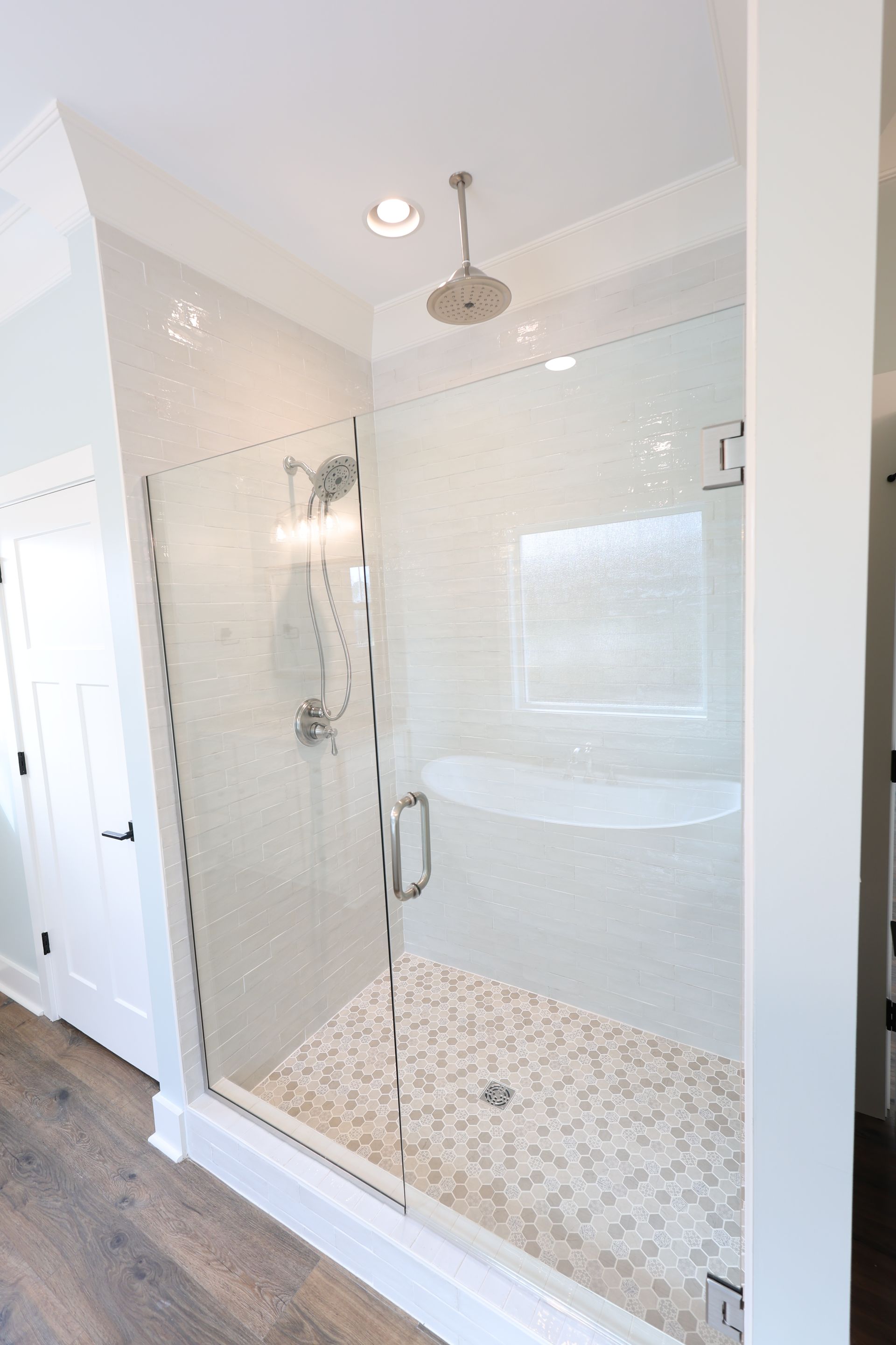 Glass-enclosed shower with pebble tile floor and white mosaic tile walls, silver shower fixtures, and a built-in bench.