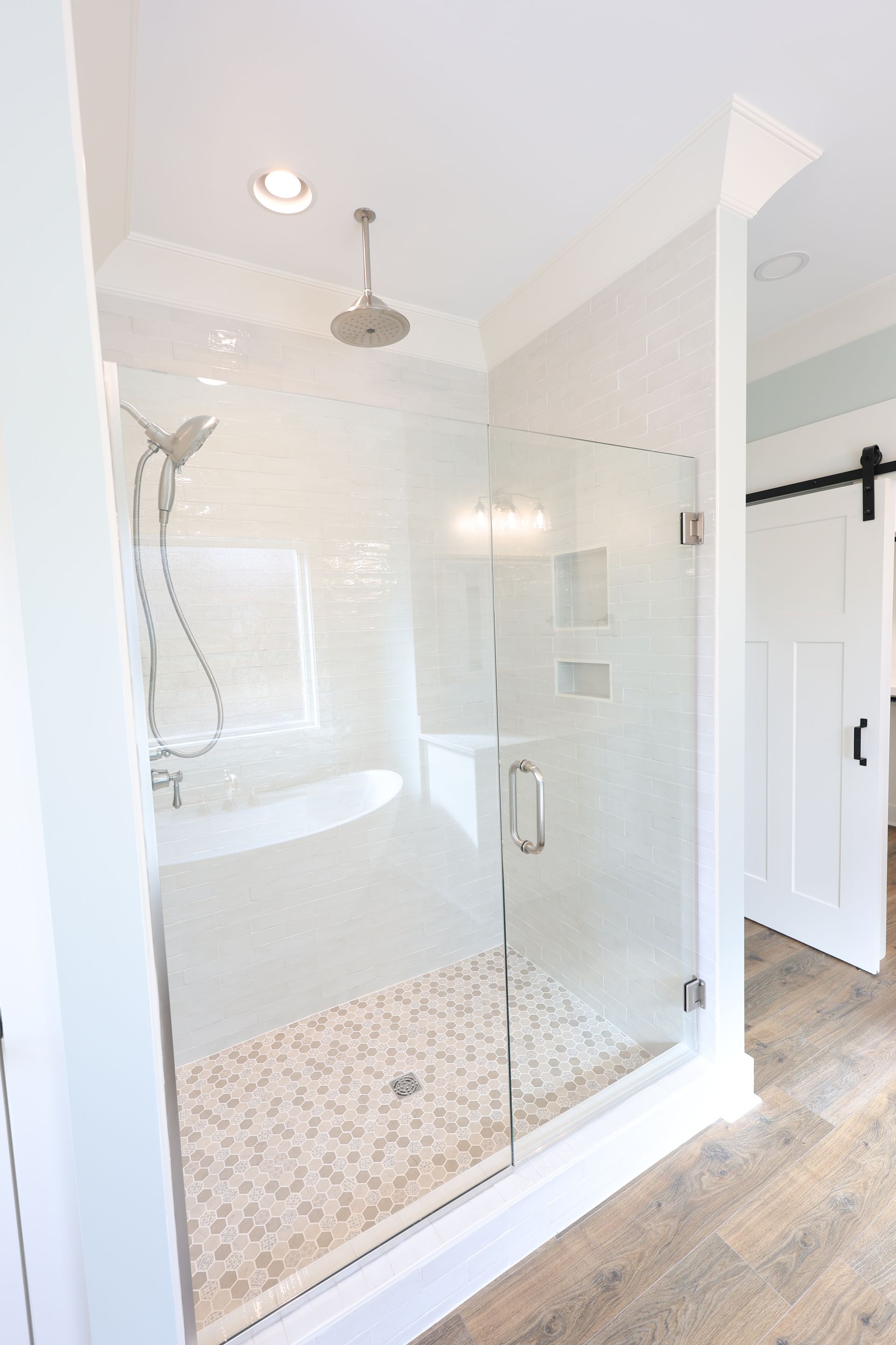 Modern, white tiled shower with glass doors, pebble floor, and rain showerhead. 