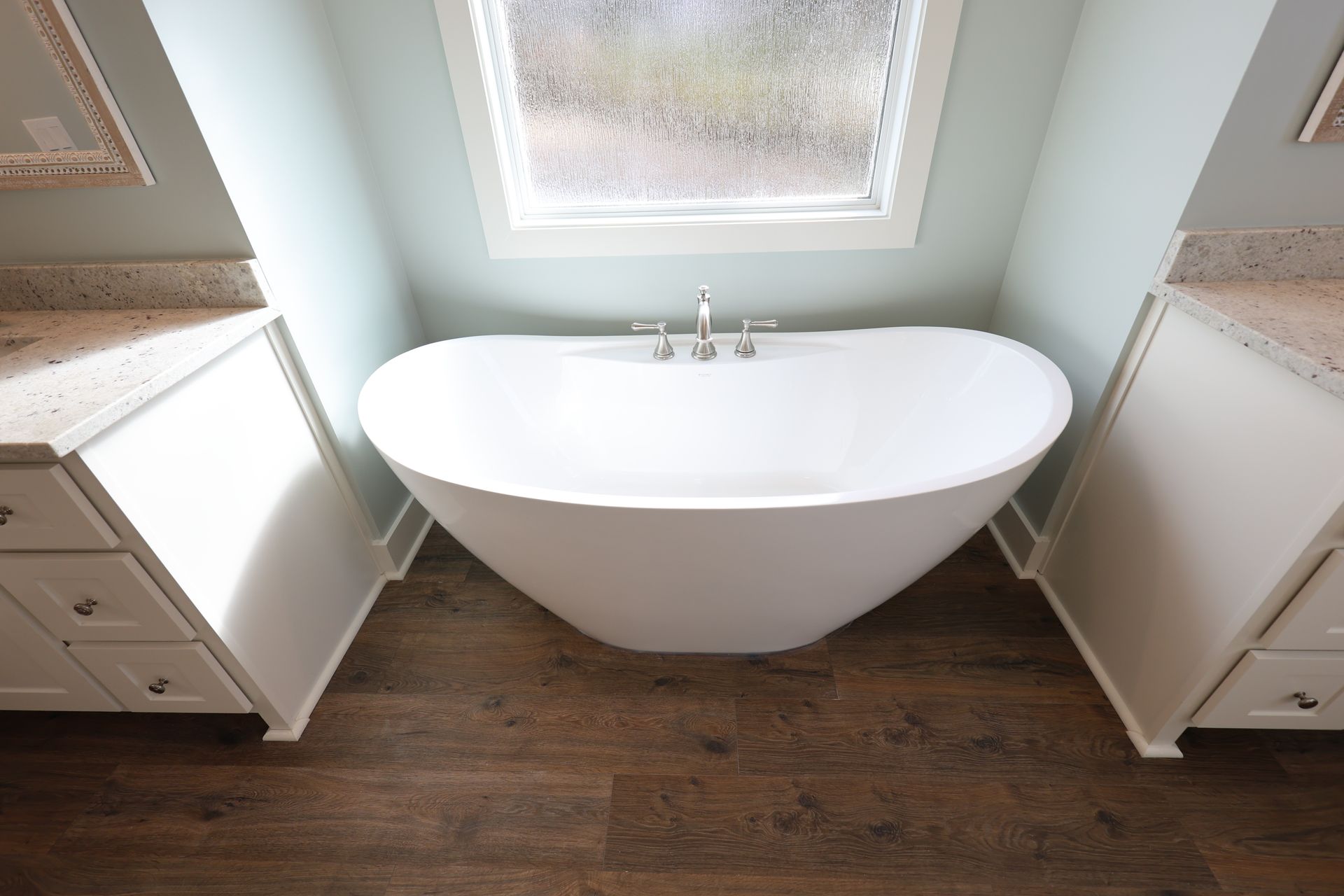White soaking tub set between two white cabinets with beige countertops, and a window.