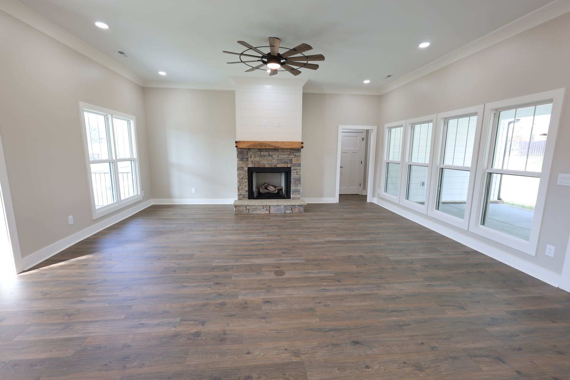 Spacious living room with fireplace, windows, ceiling fan, and hardwood floors.