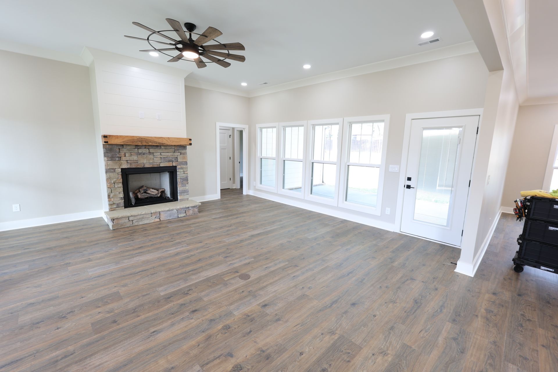 Spacious living room with stone fireplace, French doors, and hardwood floors. Ceiling fan and recessed lights.