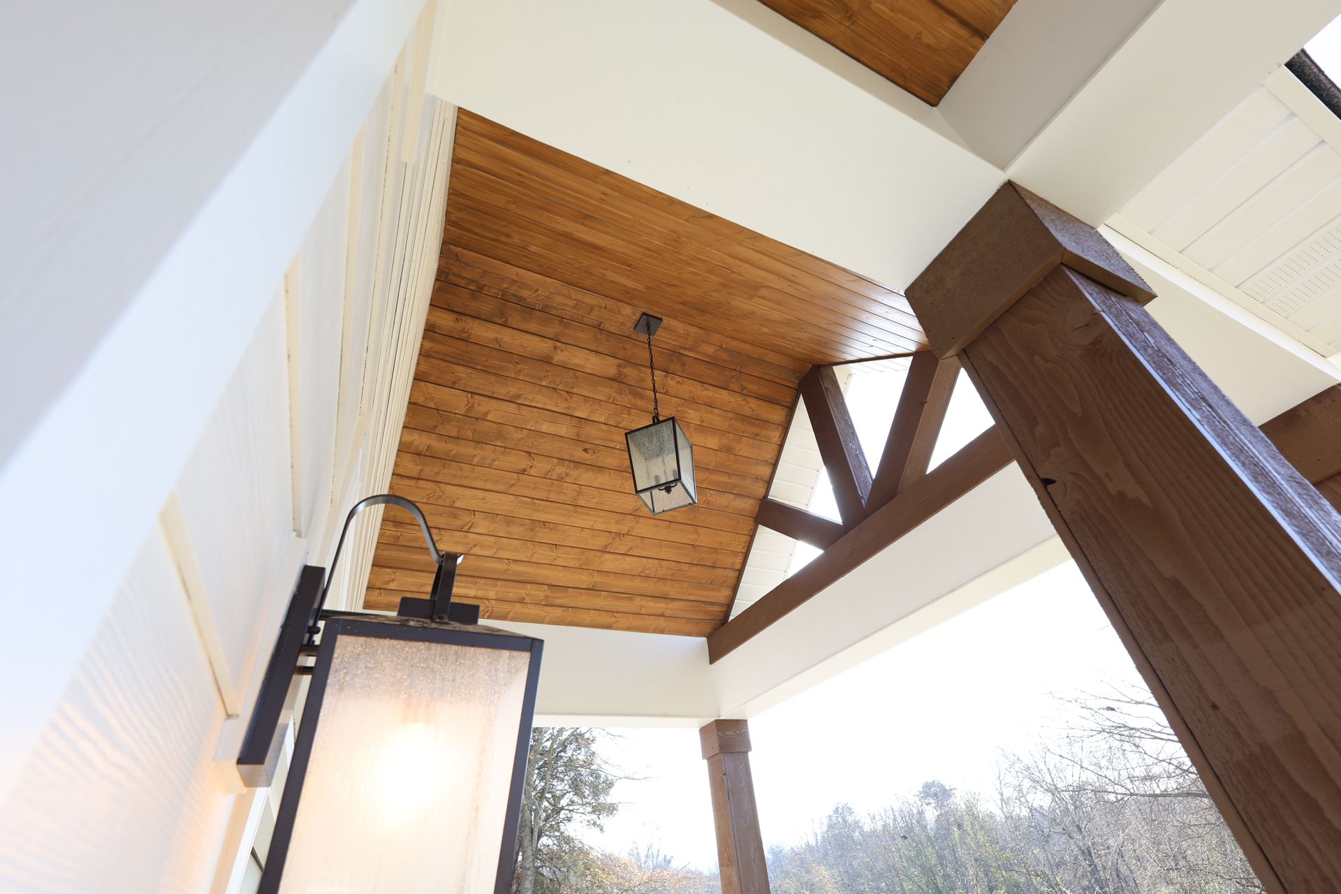 Wooden porch ceiling with a hanging light fixture and large support beams.