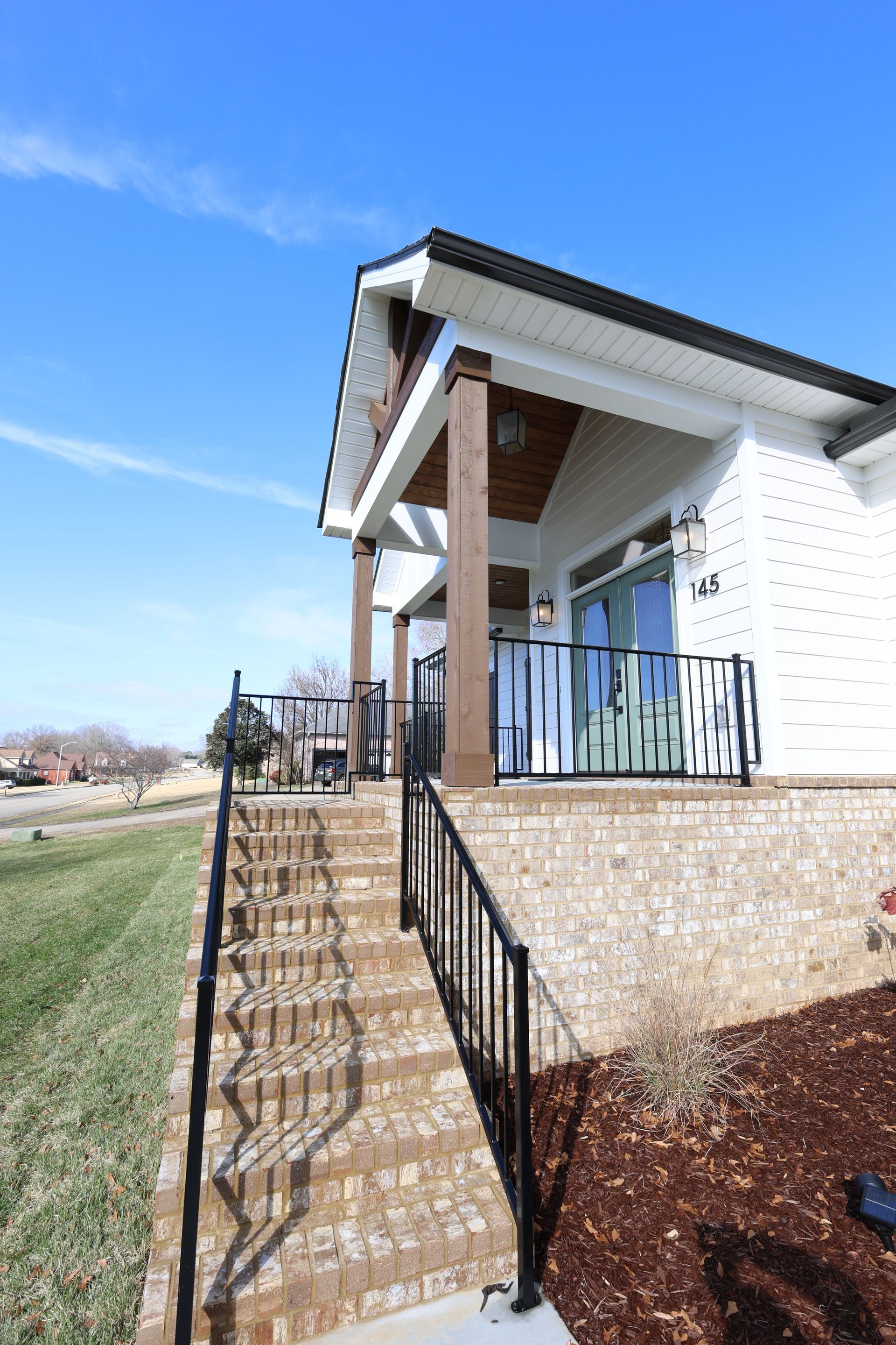 House with brick stairs, black railing, and white siding under a blue sky.