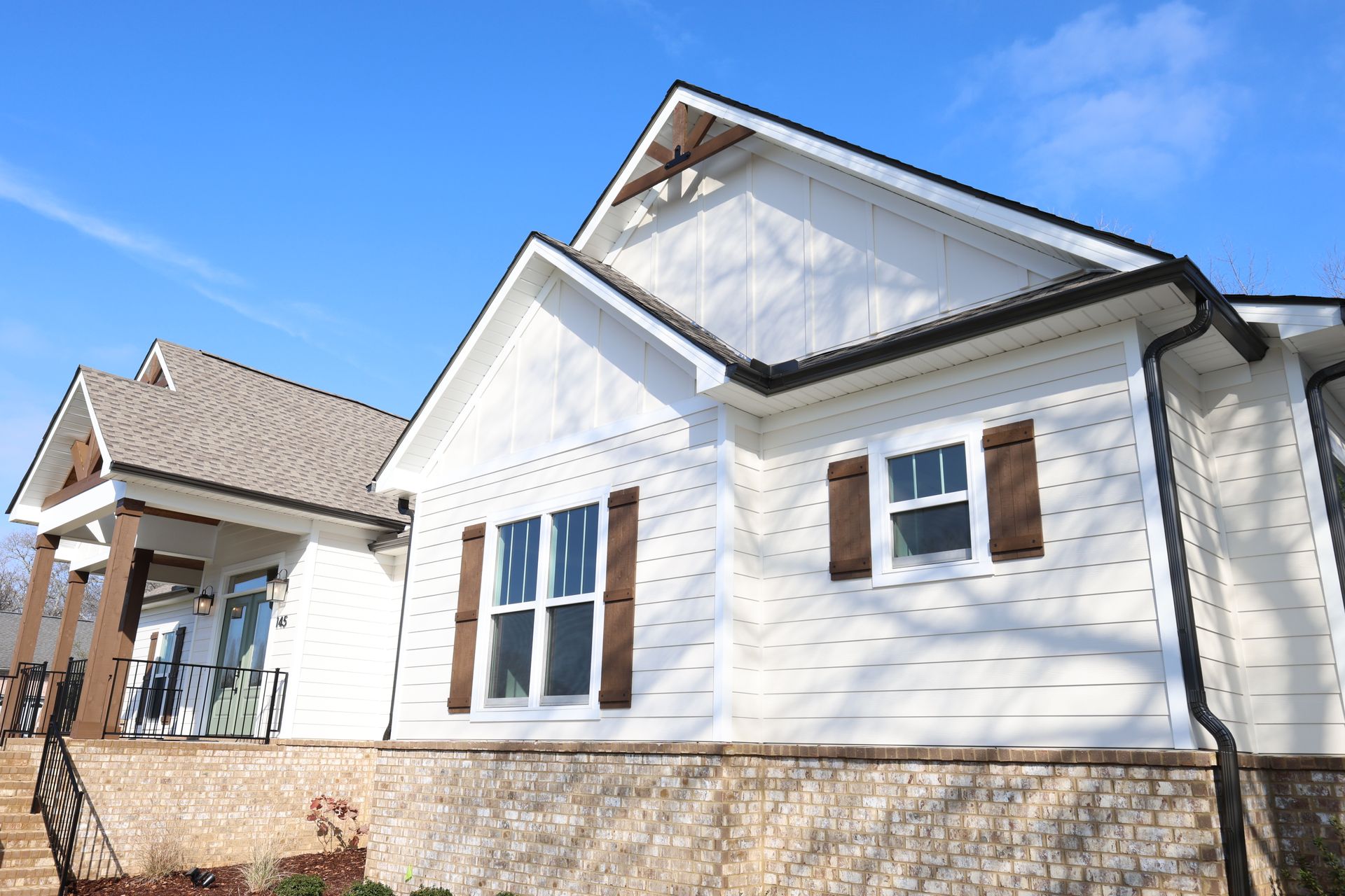 White house with brown shutters and trim, under a bright blue sky.