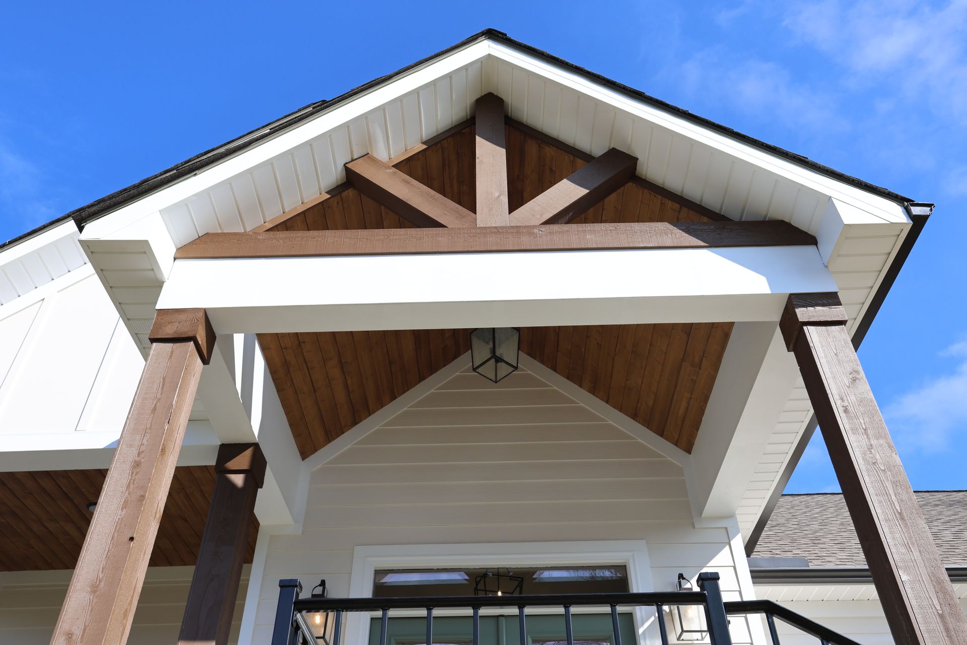 White house entrance with brown wooden beams and a peaked roof against a clear blue sky.