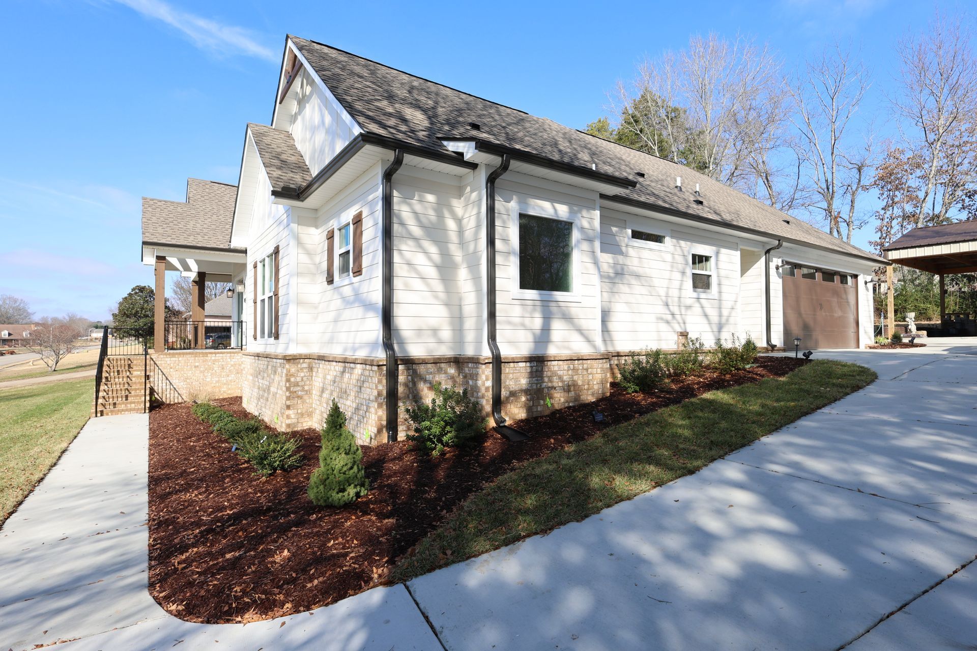 White house with brown roof, stone foundation, and driveway on a sunny day.