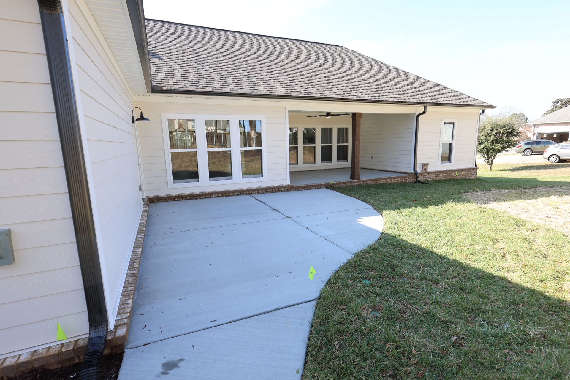 Exterior of a light beige house with a concrete patio and green lawn. Patio leads to a covered porch area.