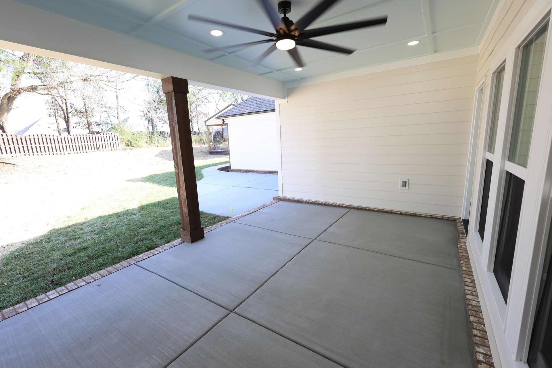 Covered outdoor patio with concrete floor, grass, and a ceiling fan.