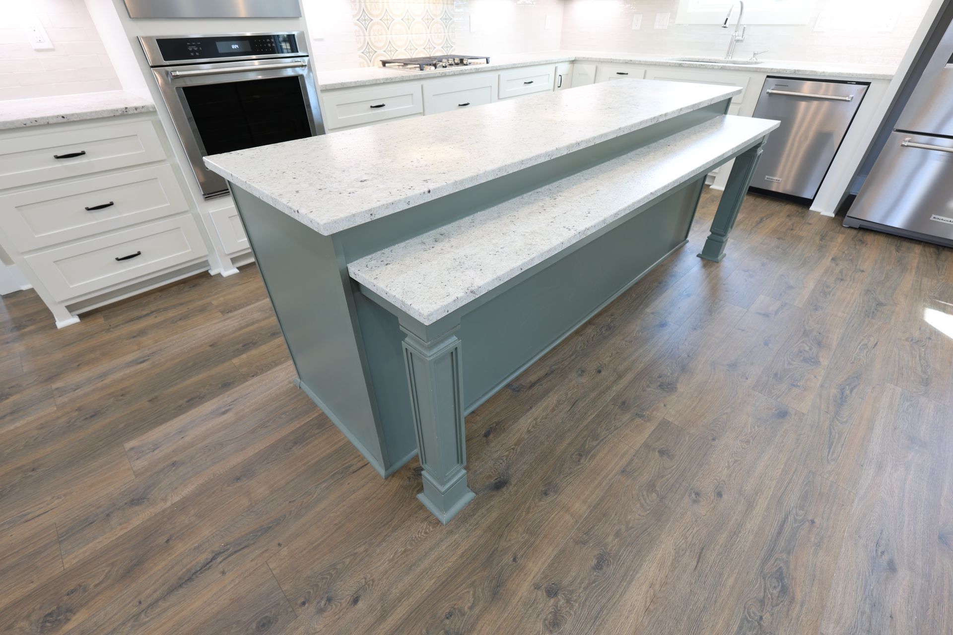 Kitchen with teal island and white countertops on wood-look floor.