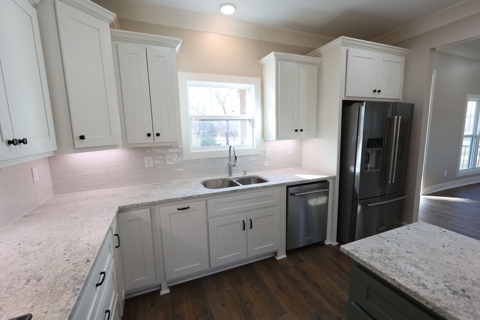 White kitchen with granite countertops, stainless steel appliances, and a window above the sink.