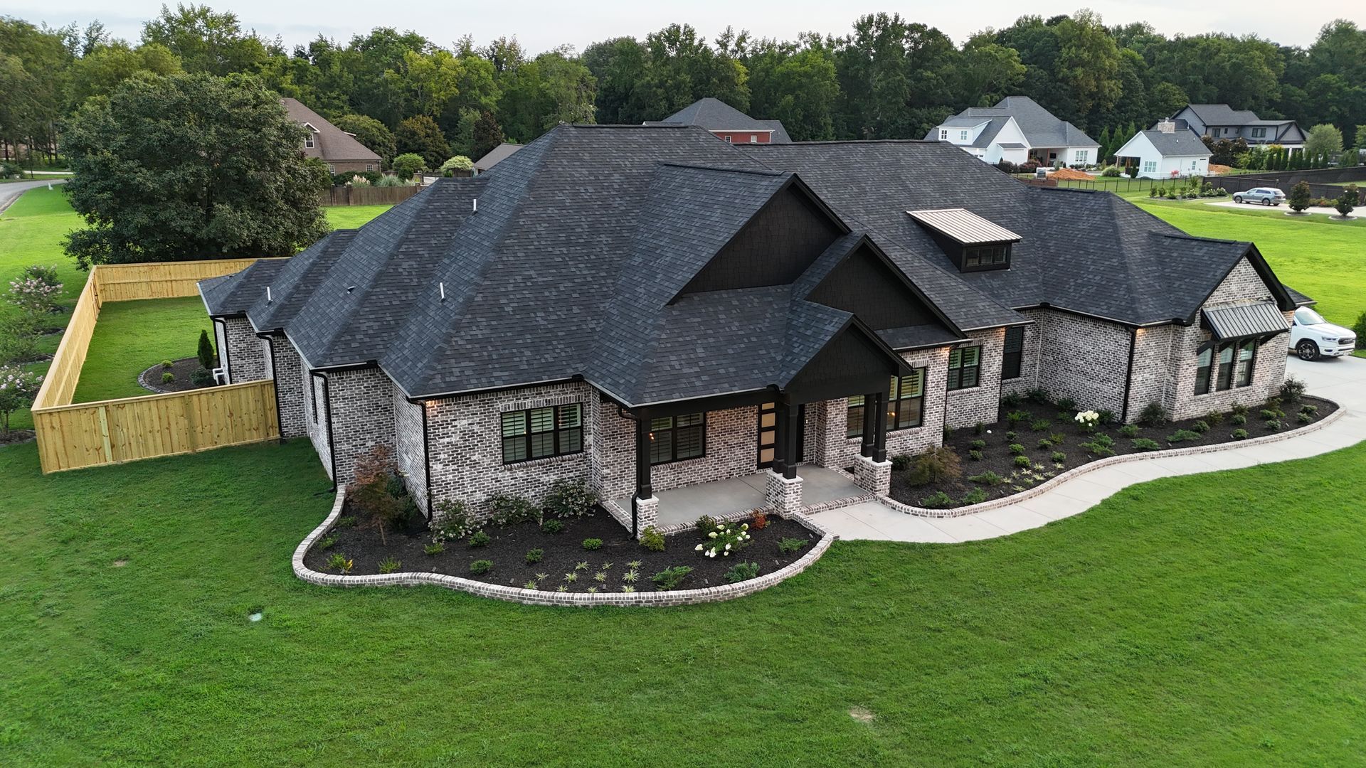 Large, modern house with a dark gray roof, brick exterior, and lush green lawn.