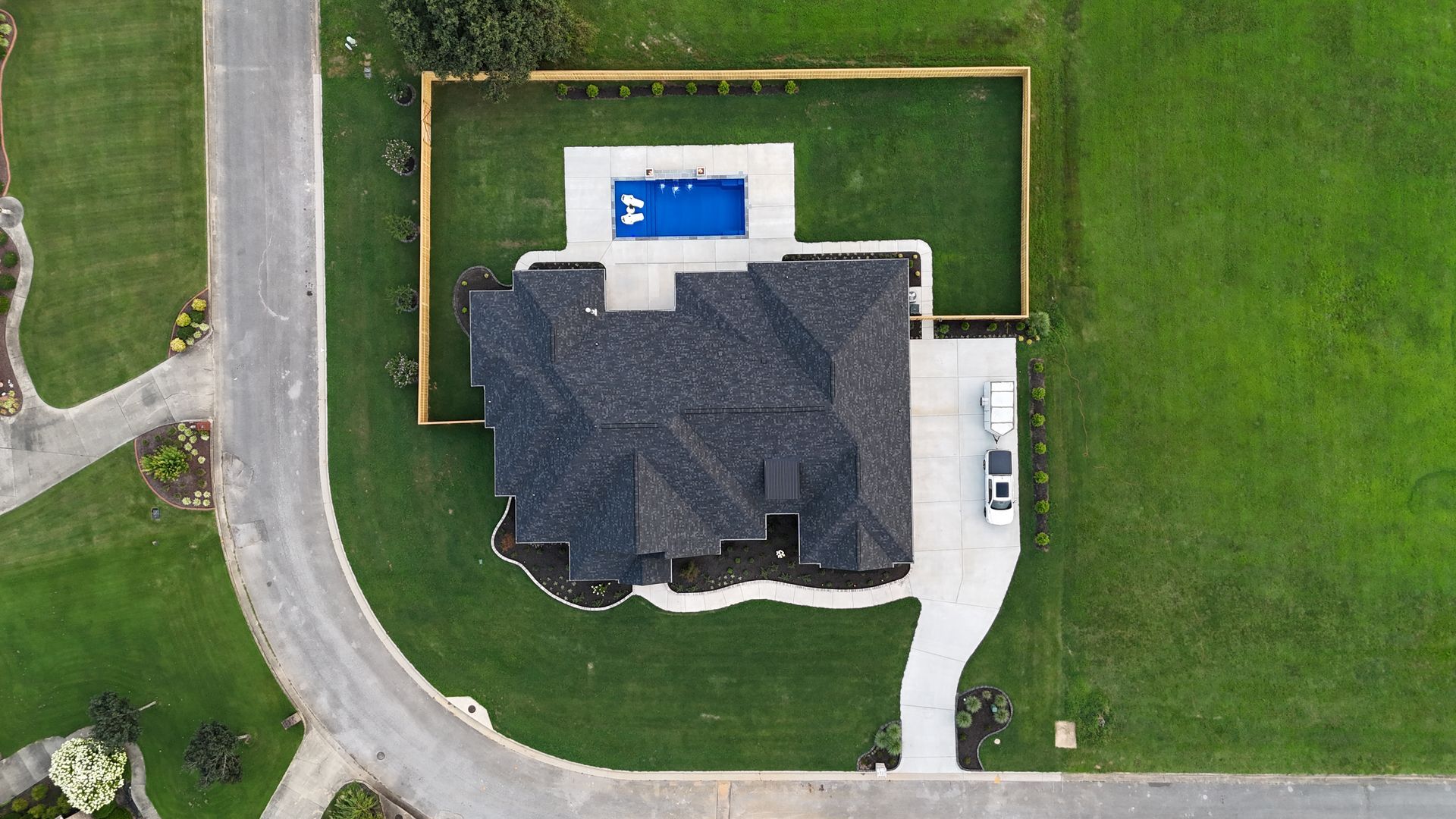 Aerial view of a house with a pool in the backyard, surrounded by a lawn and a curved driveway.