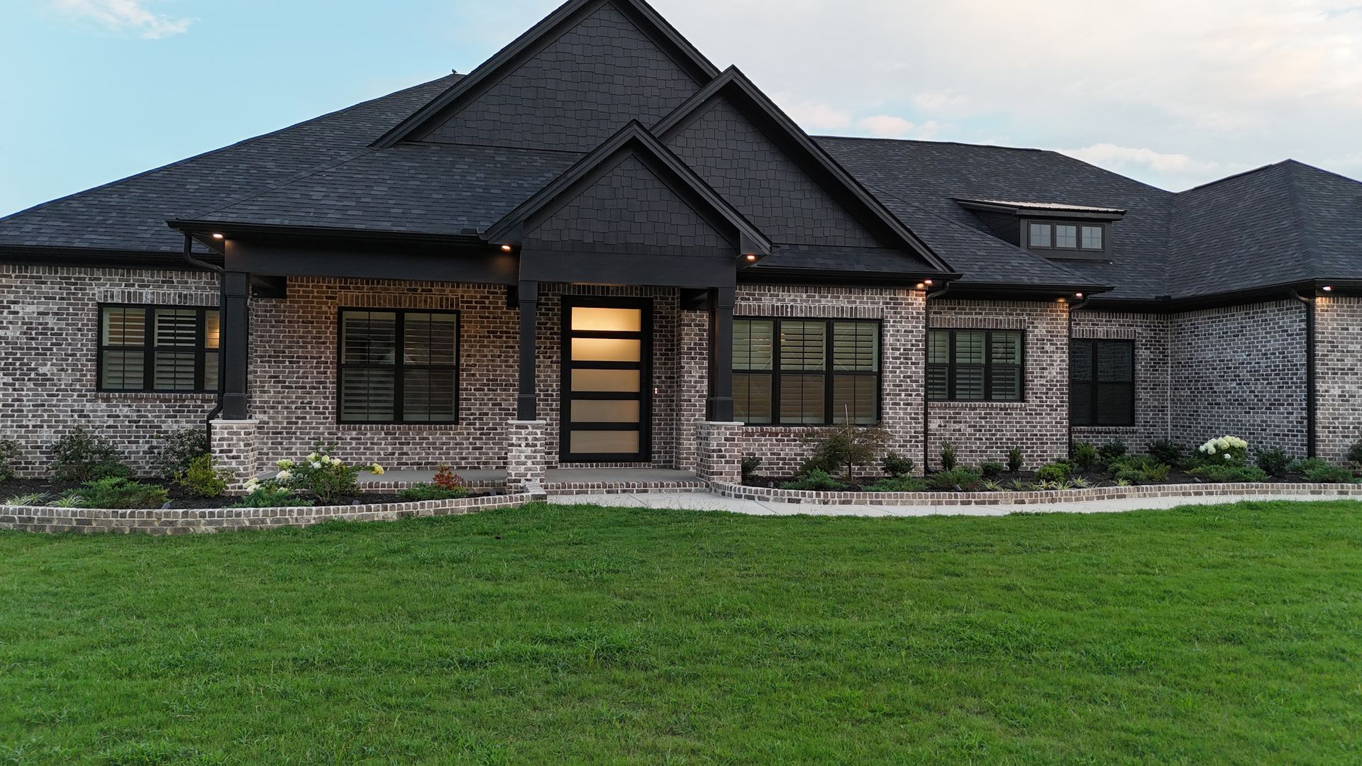 Brick house with black trim and a dark roof; green lawn in front.