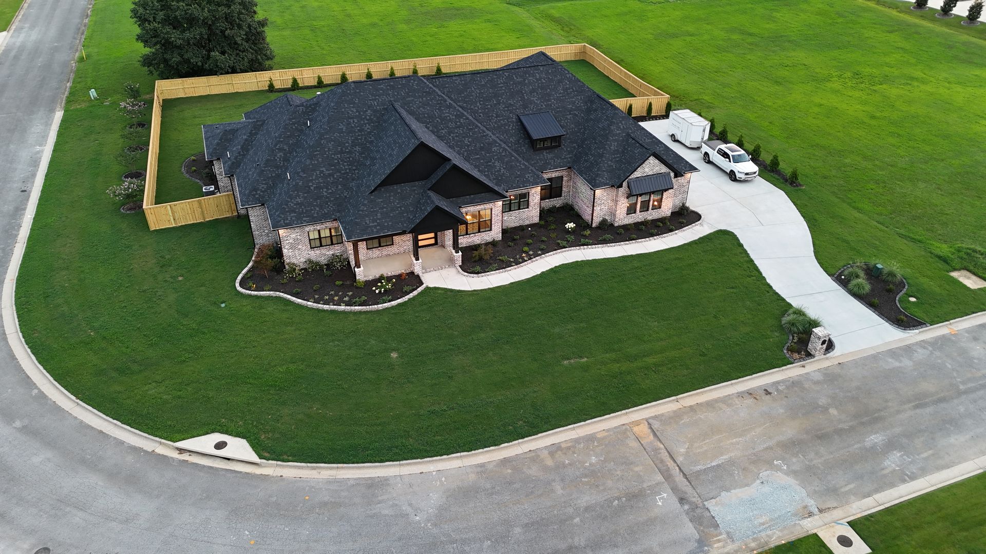 Aerial view of a large house with a black roof, stone facade, and a curved driveway on a green lawn.