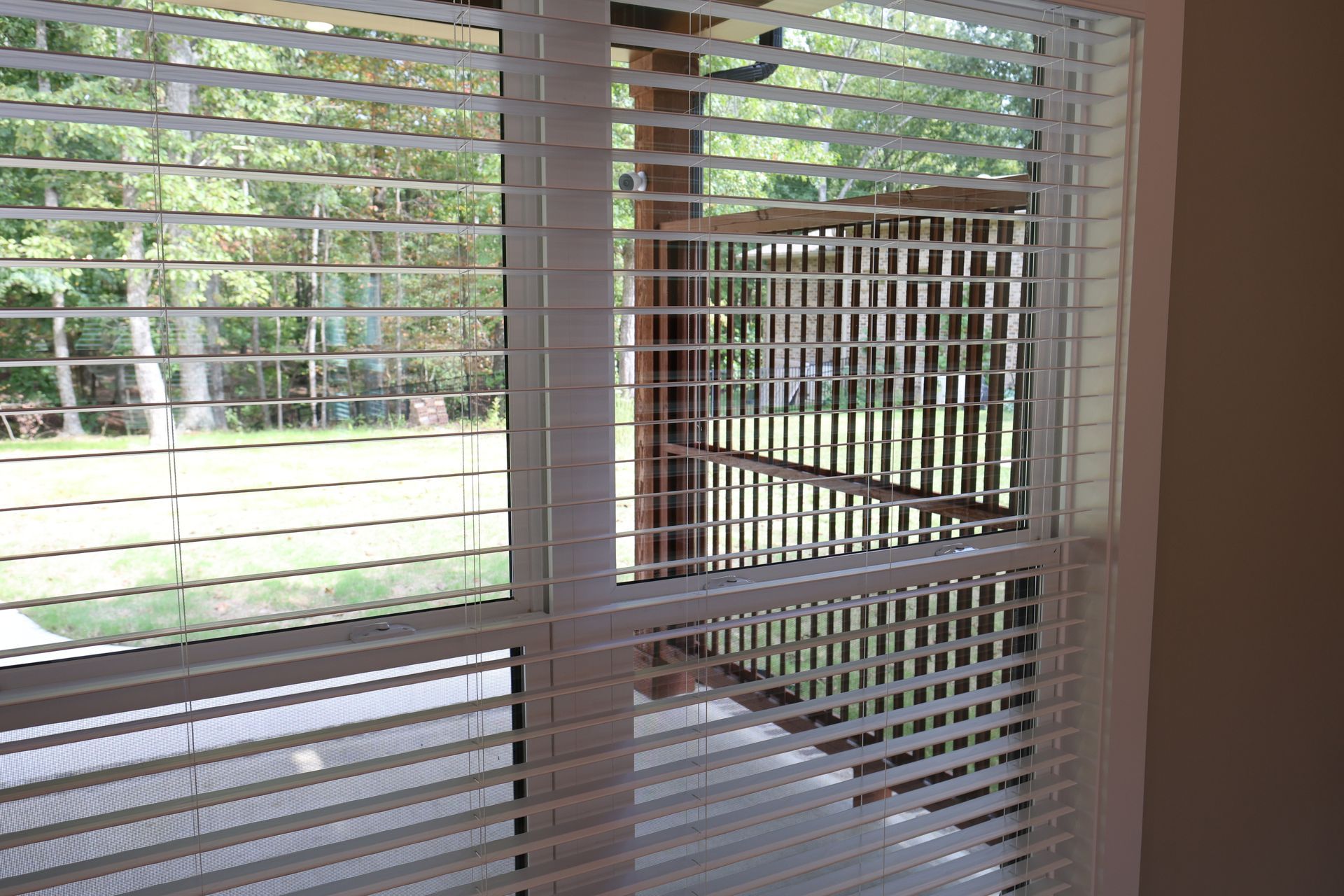 Window with white blinds, open window with a rectangular, white-grid air vent looking outside to green trees.