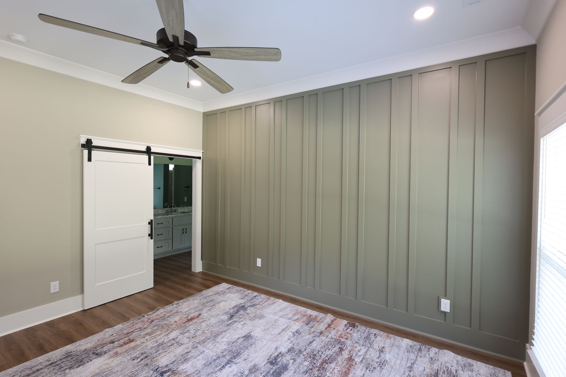 Room with olive-green paneled wall, sliding barn door, ceiling fan, and patterned rug.