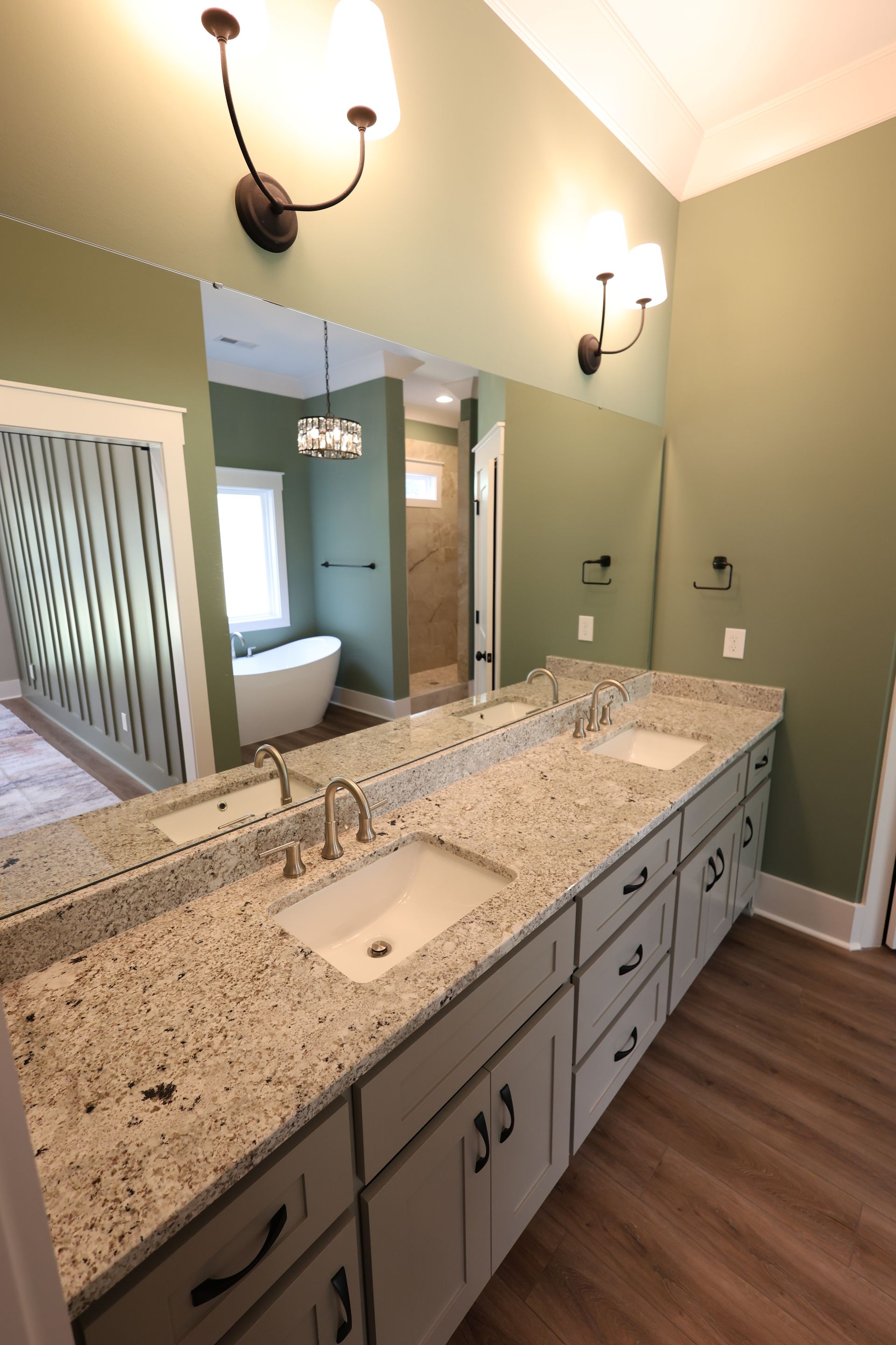 Bathroom with double sinks, large mirror, sage green walls, and light granite countertop.