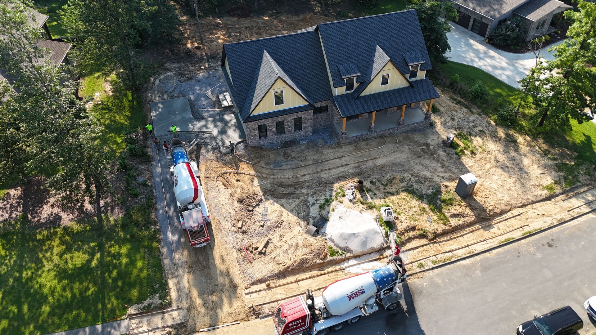 Aerial view of a house under construction; two cement trucks pour concrete near the structure.