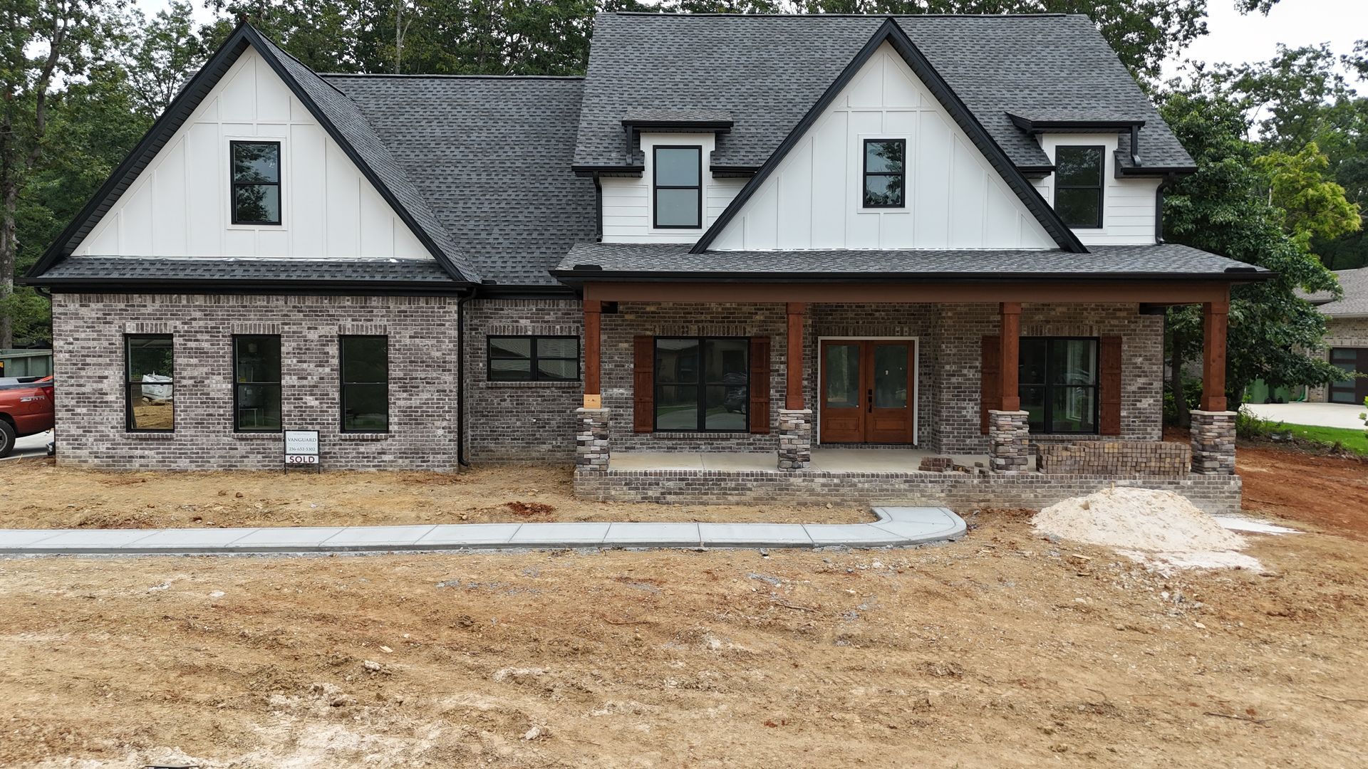 Brick and white farmhouse with a covered porch and dark gray roof, under construction.
