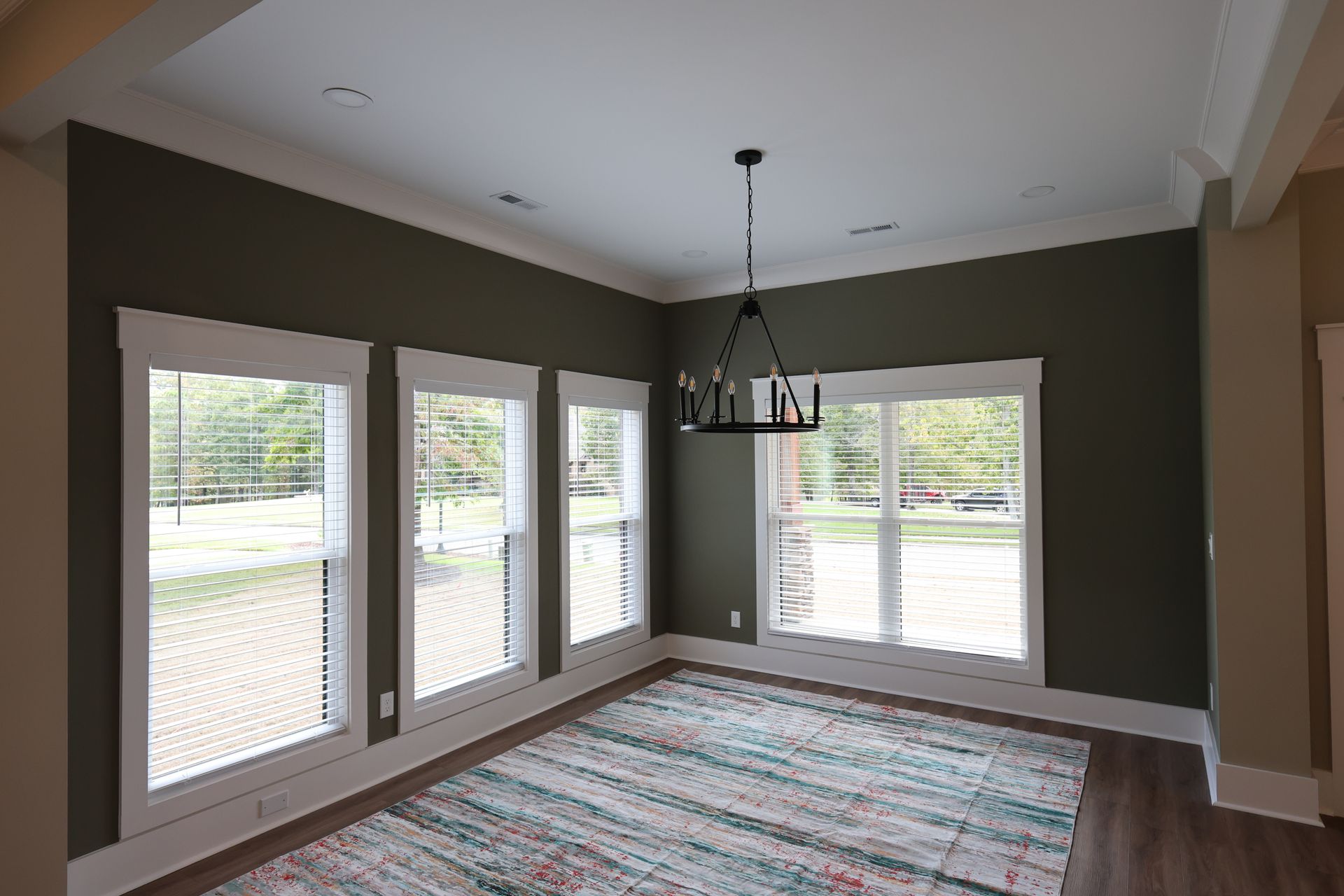 Dining room with green walls, white trim, three windows, a chandelier, and a colorful rug.
