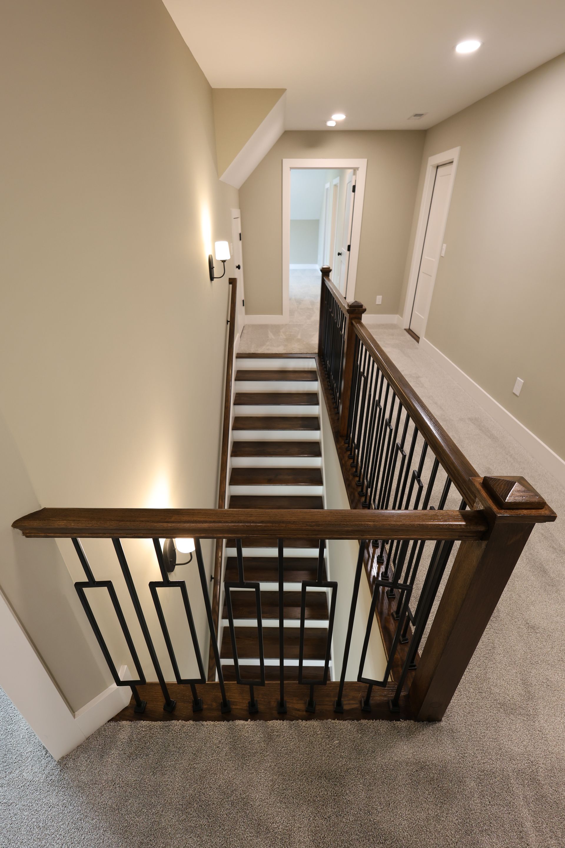 Staircase with dark wood steps and railing, beige walls, and light gray carpet.