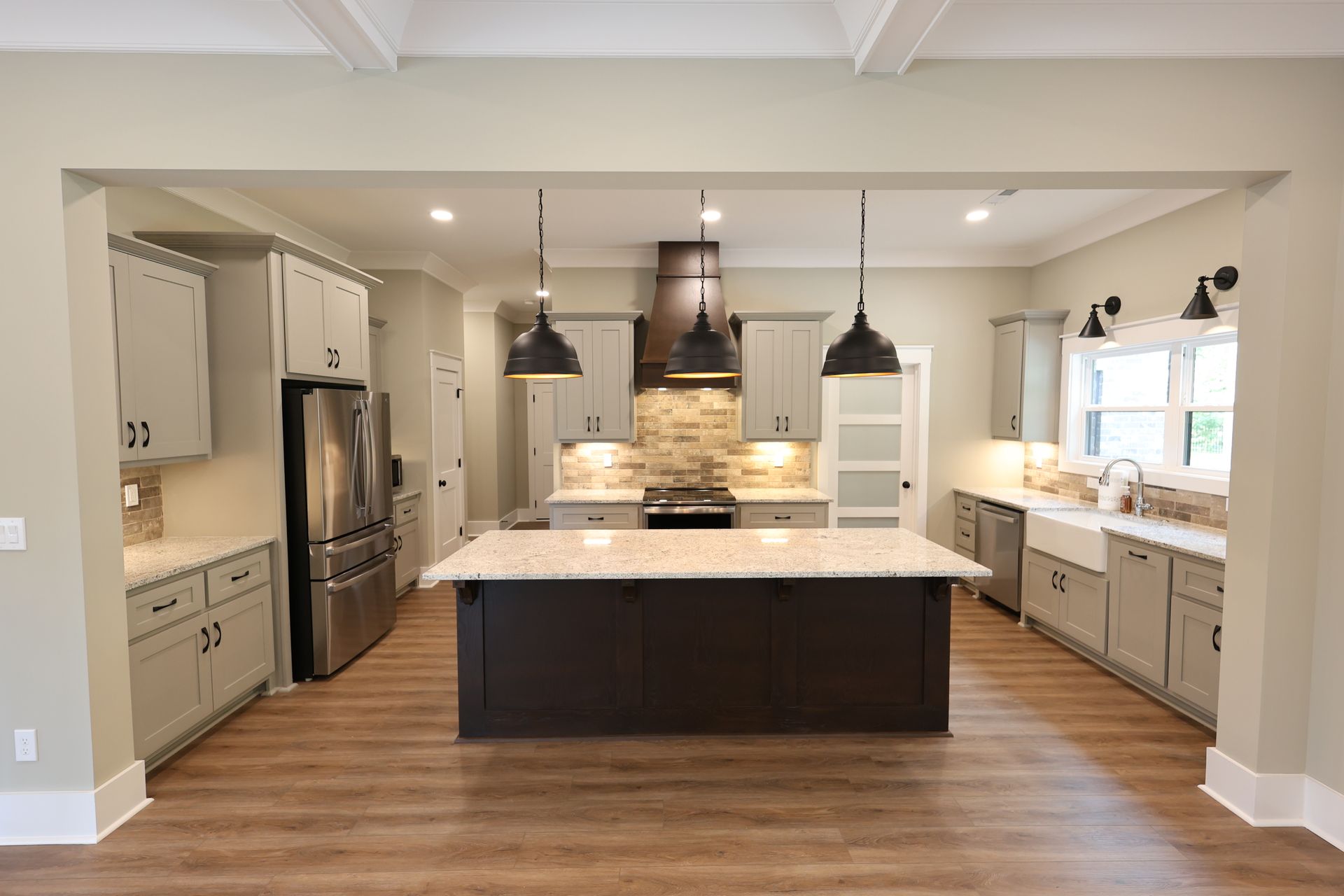 Kitchen with gray cabinets, dark island, stainless steel appliances, and pendant lights.