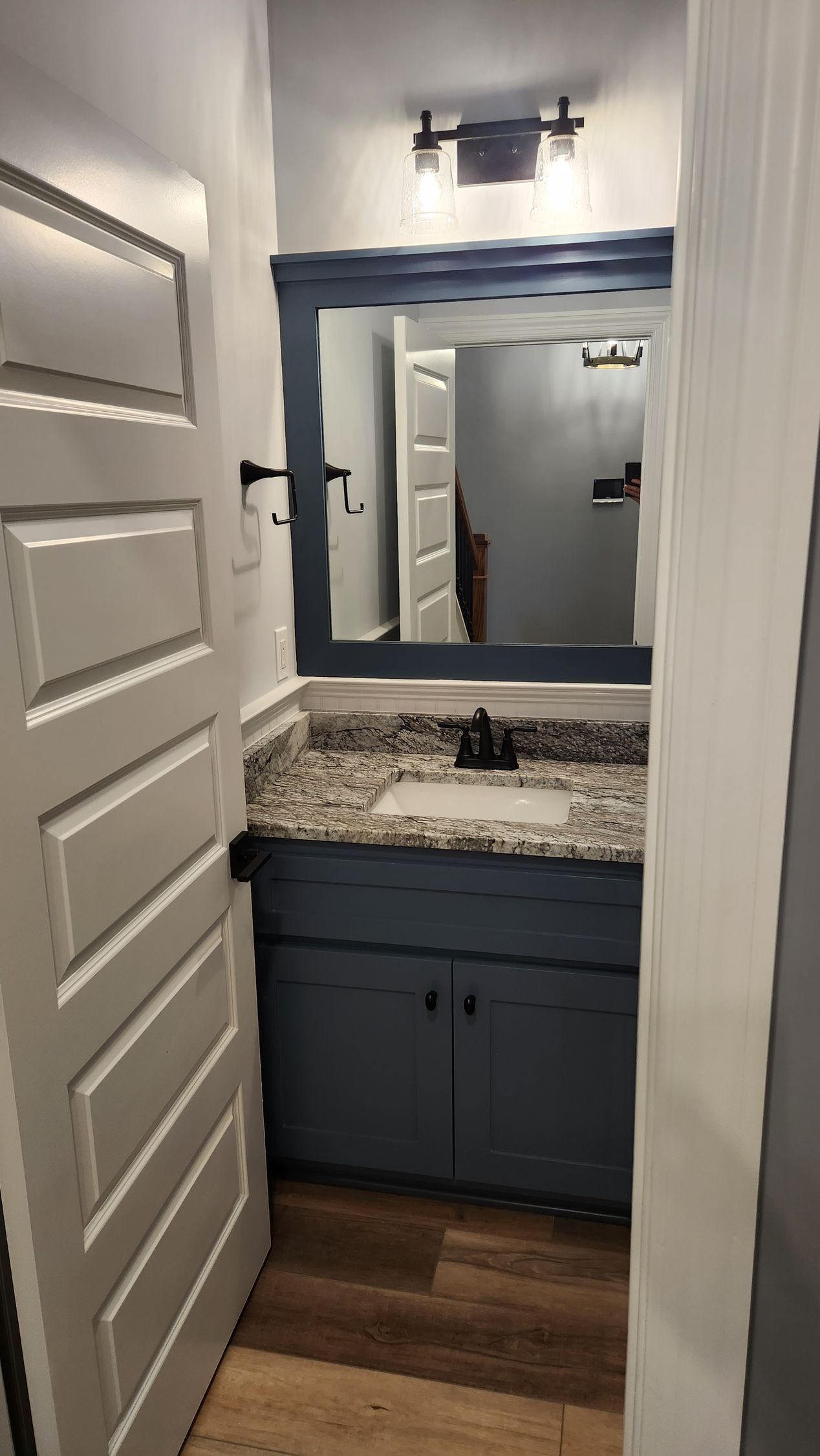 Small bathroom with blue vanity and mirror frame, granite countertop, white door.