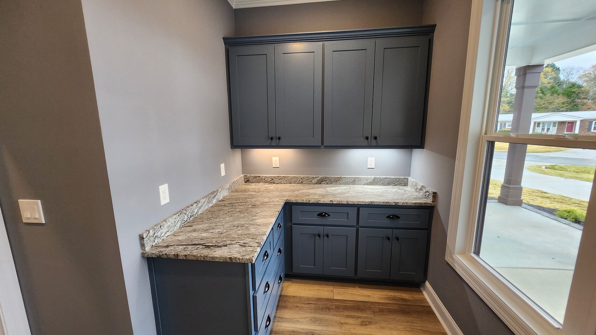 Blue cabinets with a gray granite countertop in a corner nook, near a window.