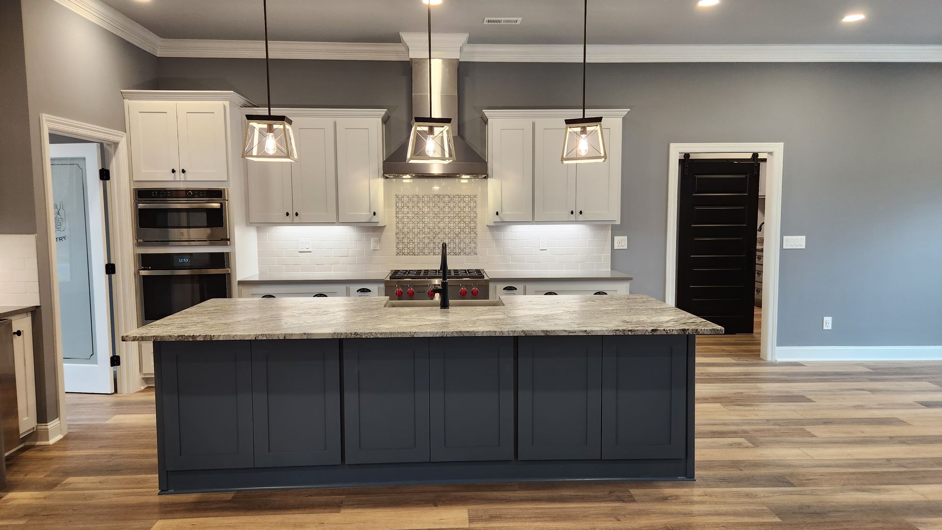 Modern kitchen with grey and white cabinets, large island, stainless steel appliances, and wooden floors.