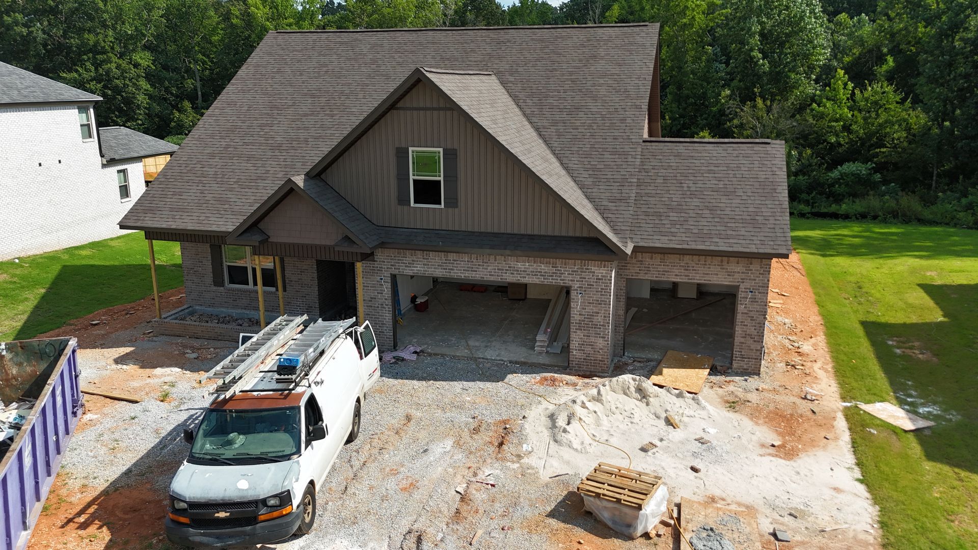 New house under construction with brick facade, two-car garage, and brown roof. A work van is parked in front.