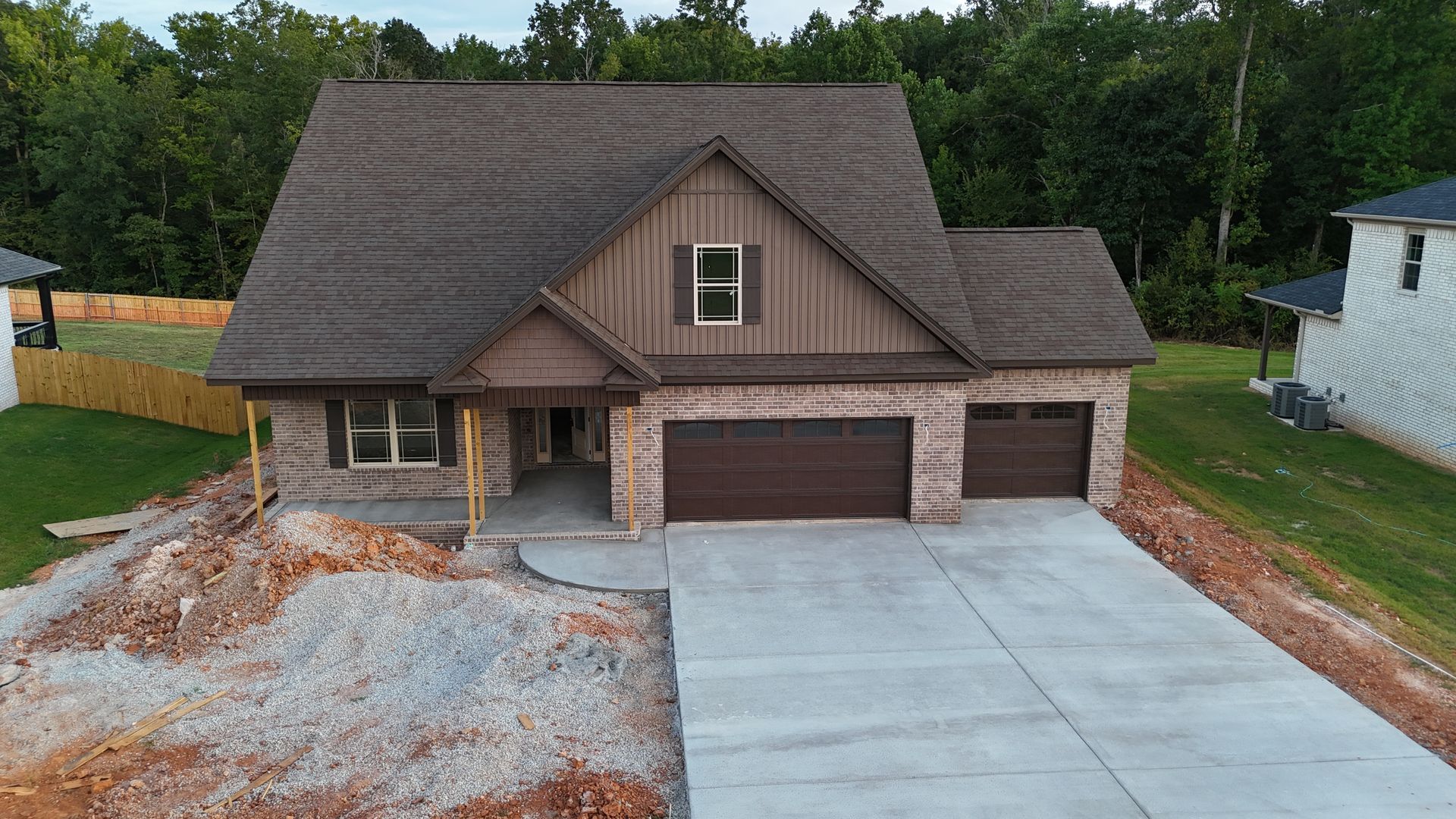 New brick house with brown roof and garage doors, concrete driveway, and construction debris.
