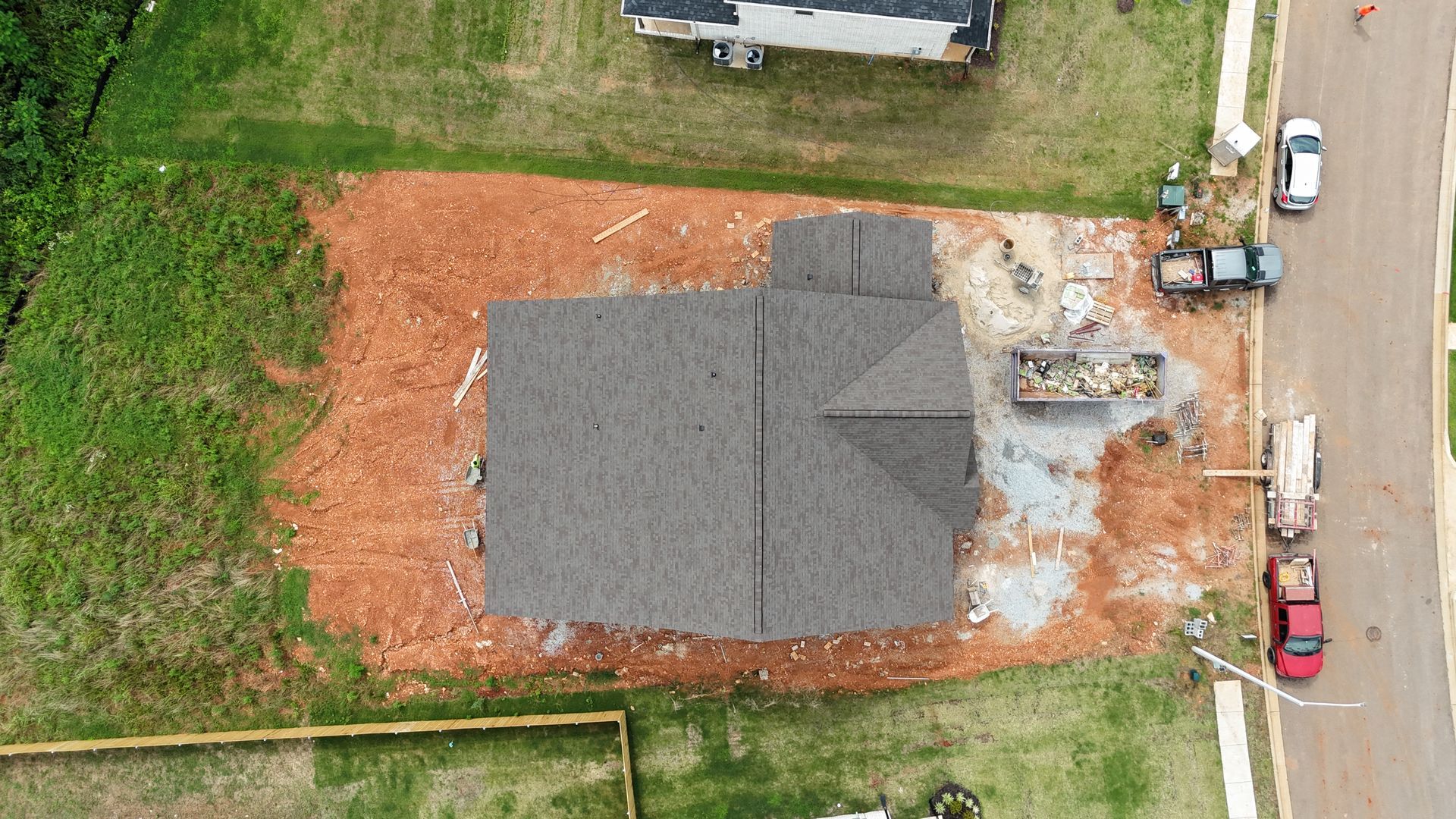 Aerial view of house under construction; roof completed, surrounded by red dirt and construction materials.
