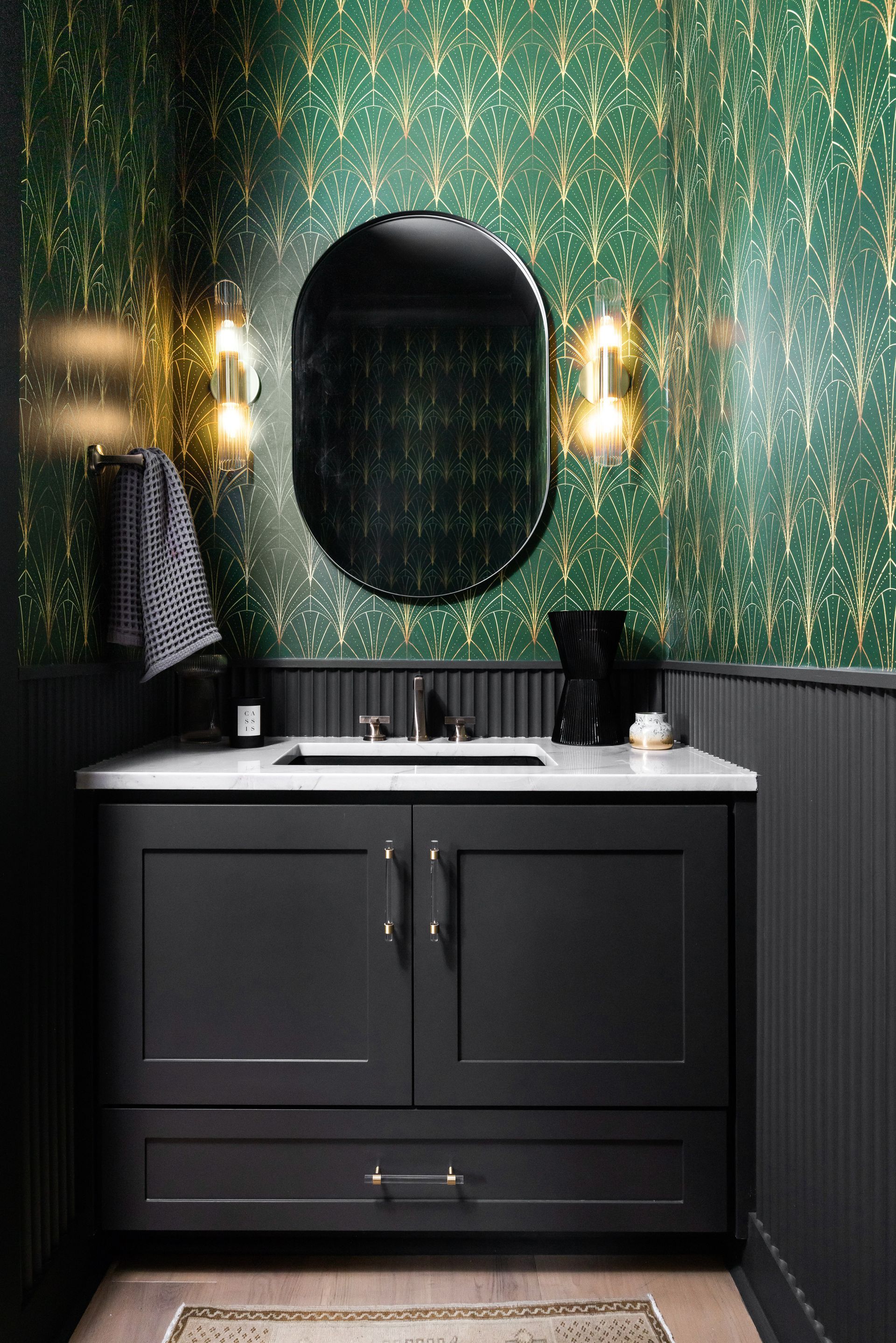Bathroom with green and gold wallpaper, black vanity, and oval mirror.