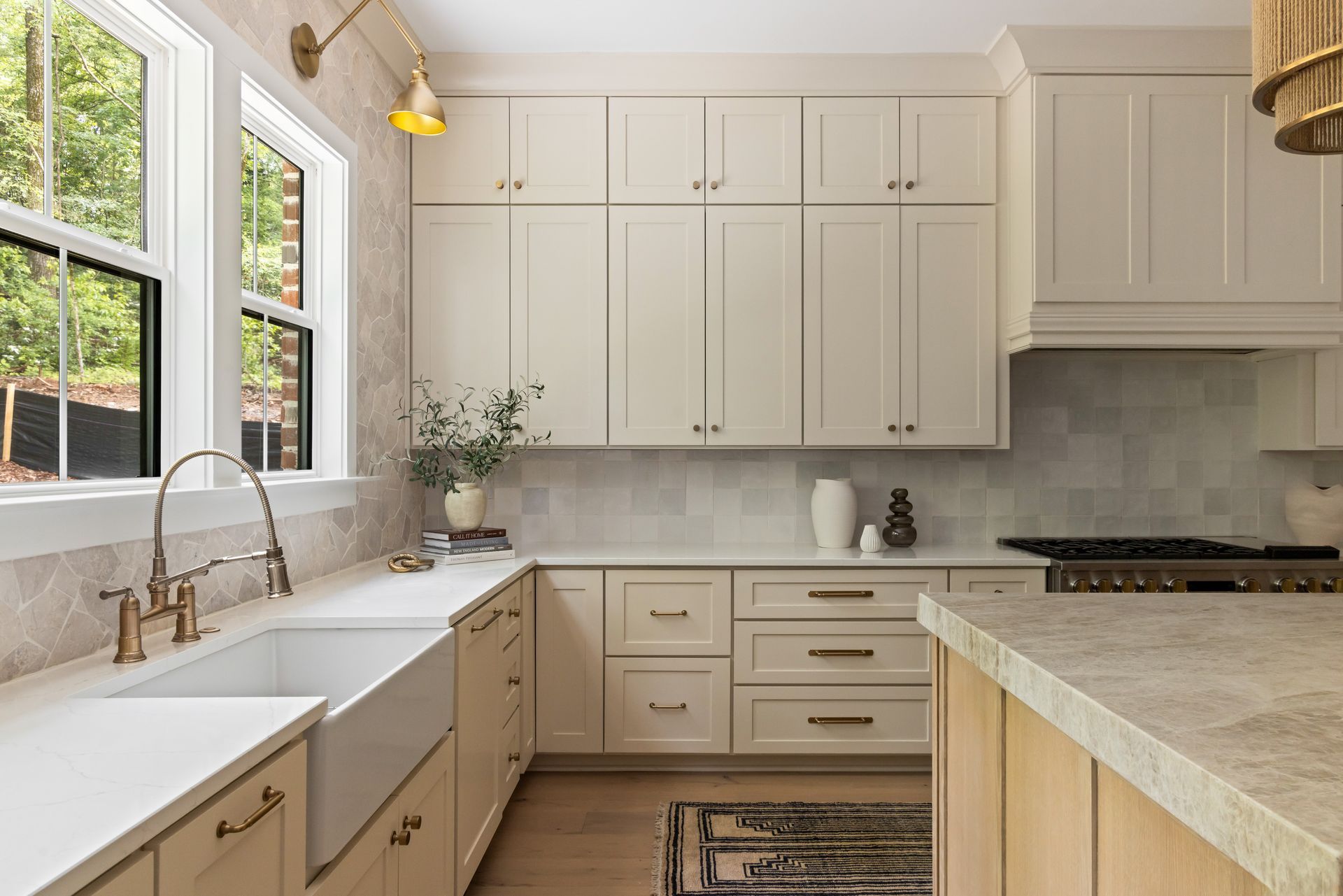Cream-colored kitchen with white countertops, light brown cabinets, and a farmhouse sink near windows.