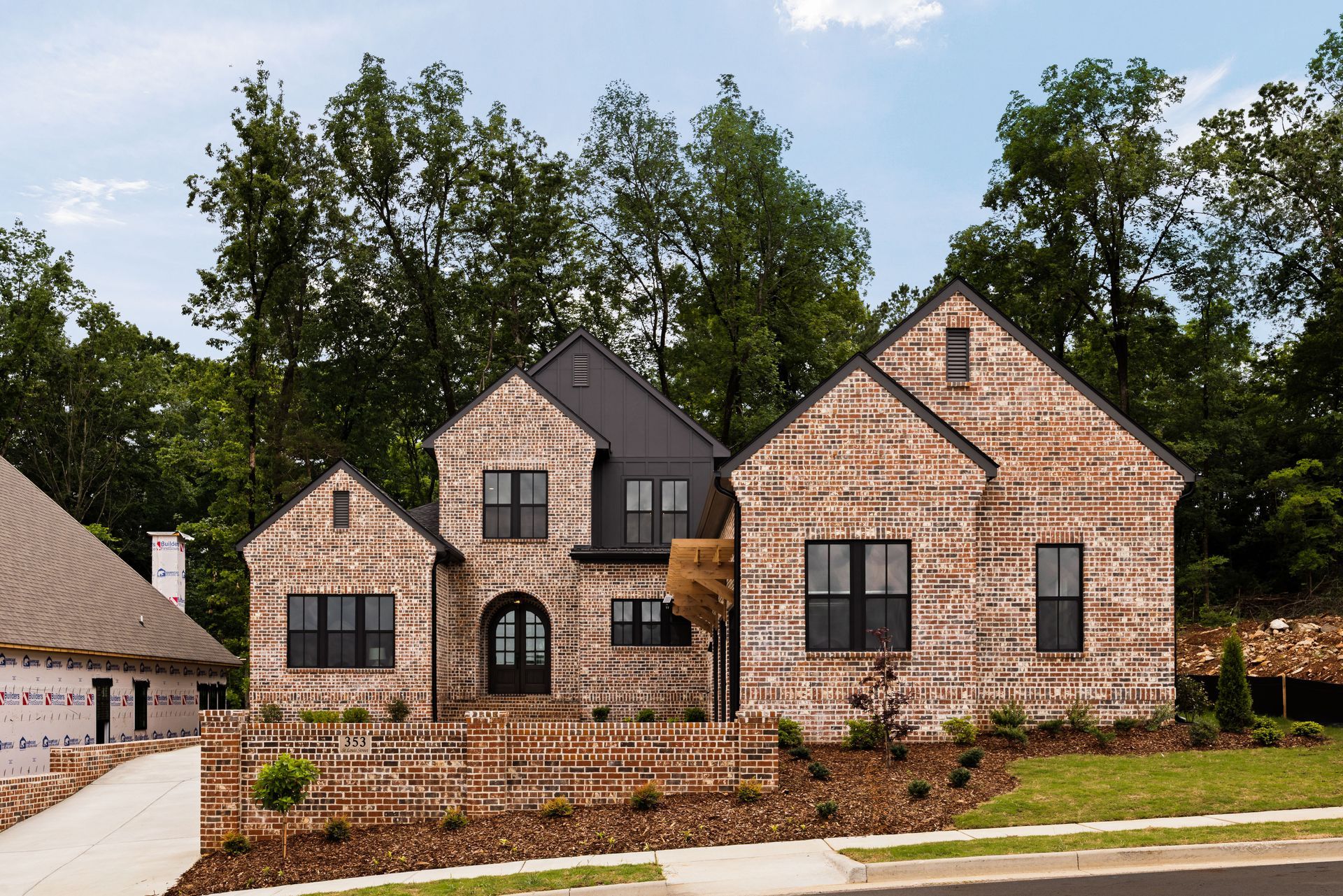 Brick house with black trim and roof, set among trees and shrubs.