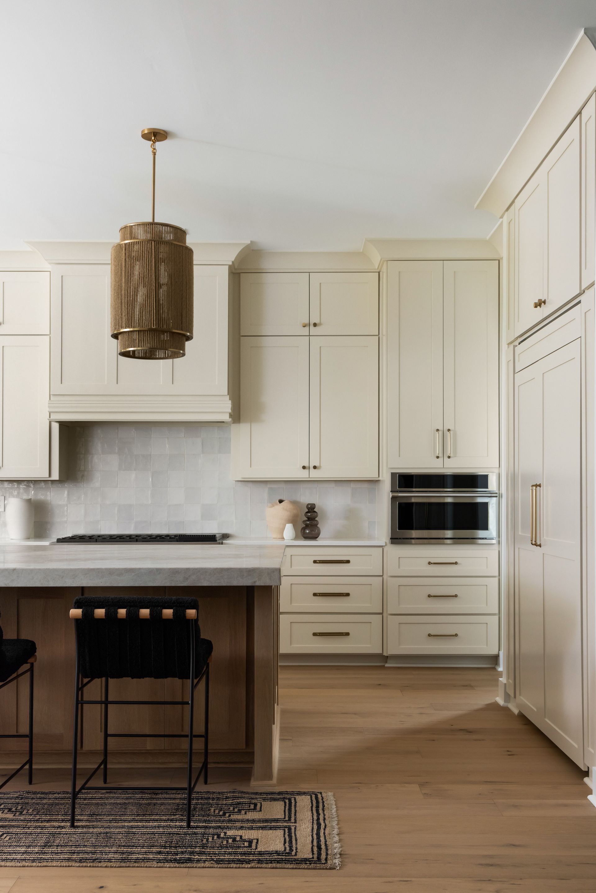 Cream-colored kitchen with wood floors, island, and cabinets. A decorative light fixture hangs above the island.