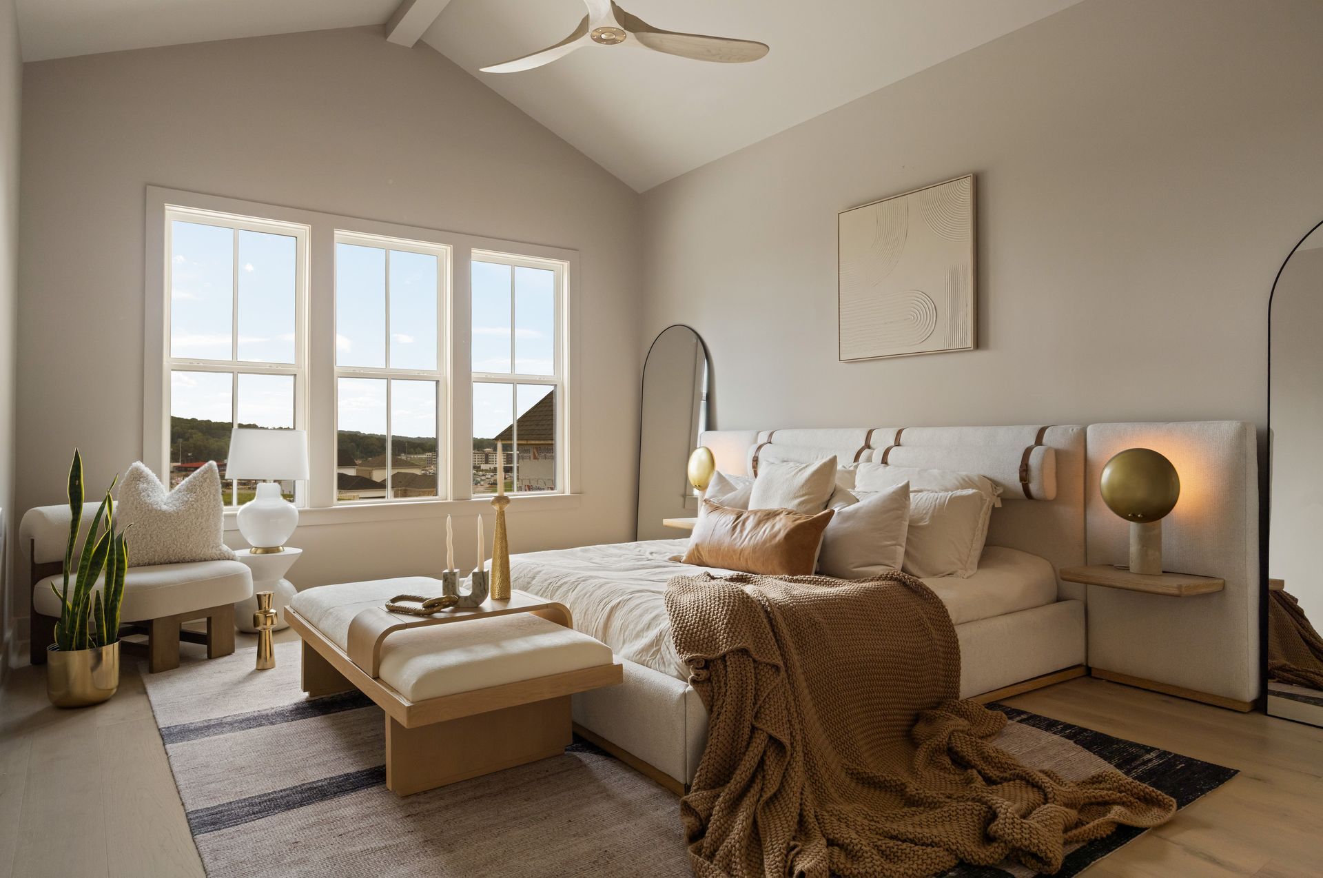 Neutral-toned bedroom with bed, two mirrors, bench, and window overlooking a mountain range.