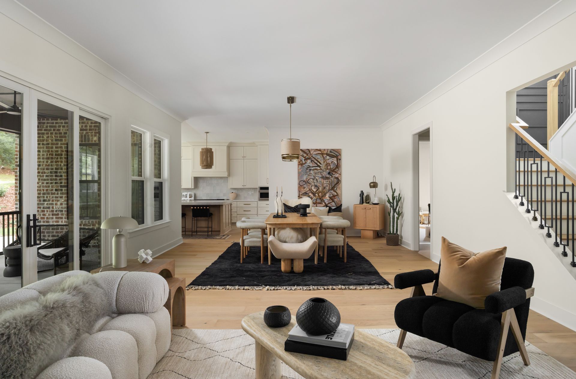 Open-plan living space with kitchen, dining area, and living room. Light wood floors, black rug, and cream walls.