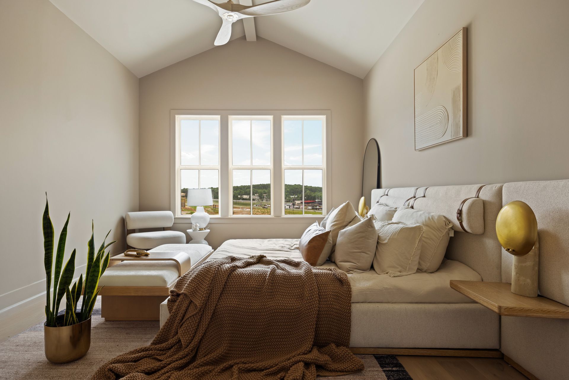 Bedroom with beige walls, a bed, a window with a view, and decorative elements.
