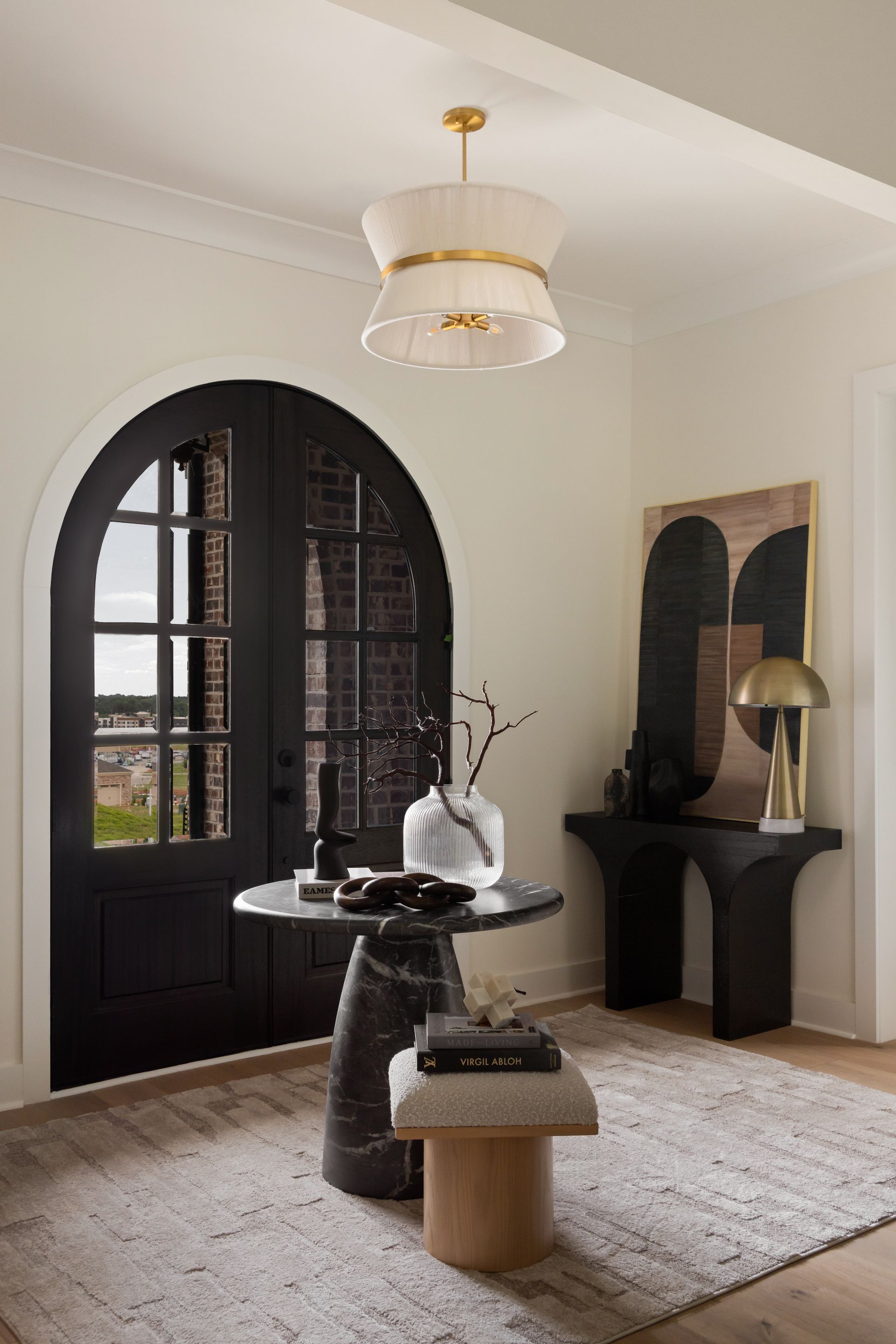 Elegant entryway with black arched door, black and marble table, console table with art, and a light fixture.