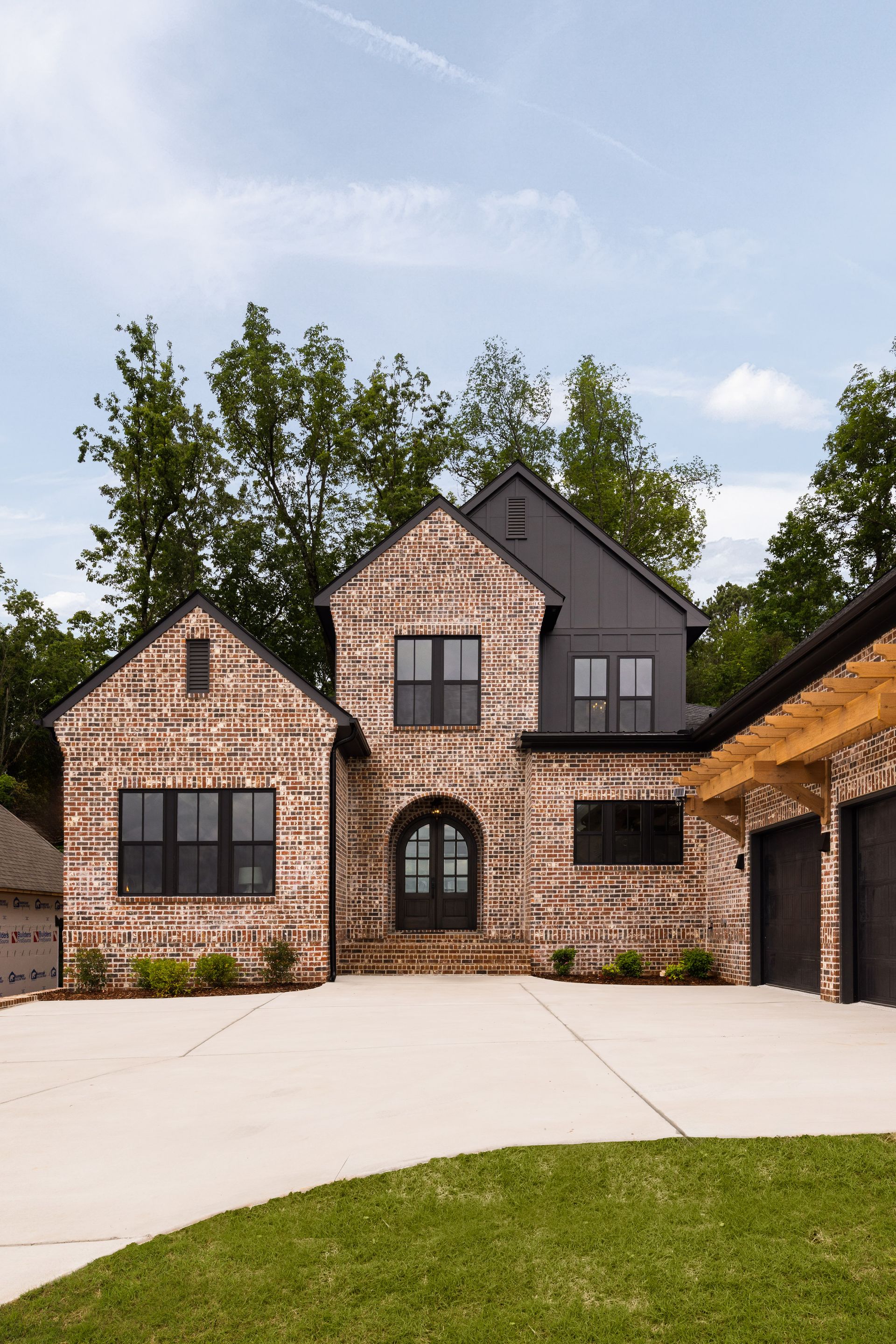 Brick home with black windows, garage doors, and accents, set on a green lawn with a concrete driveway.