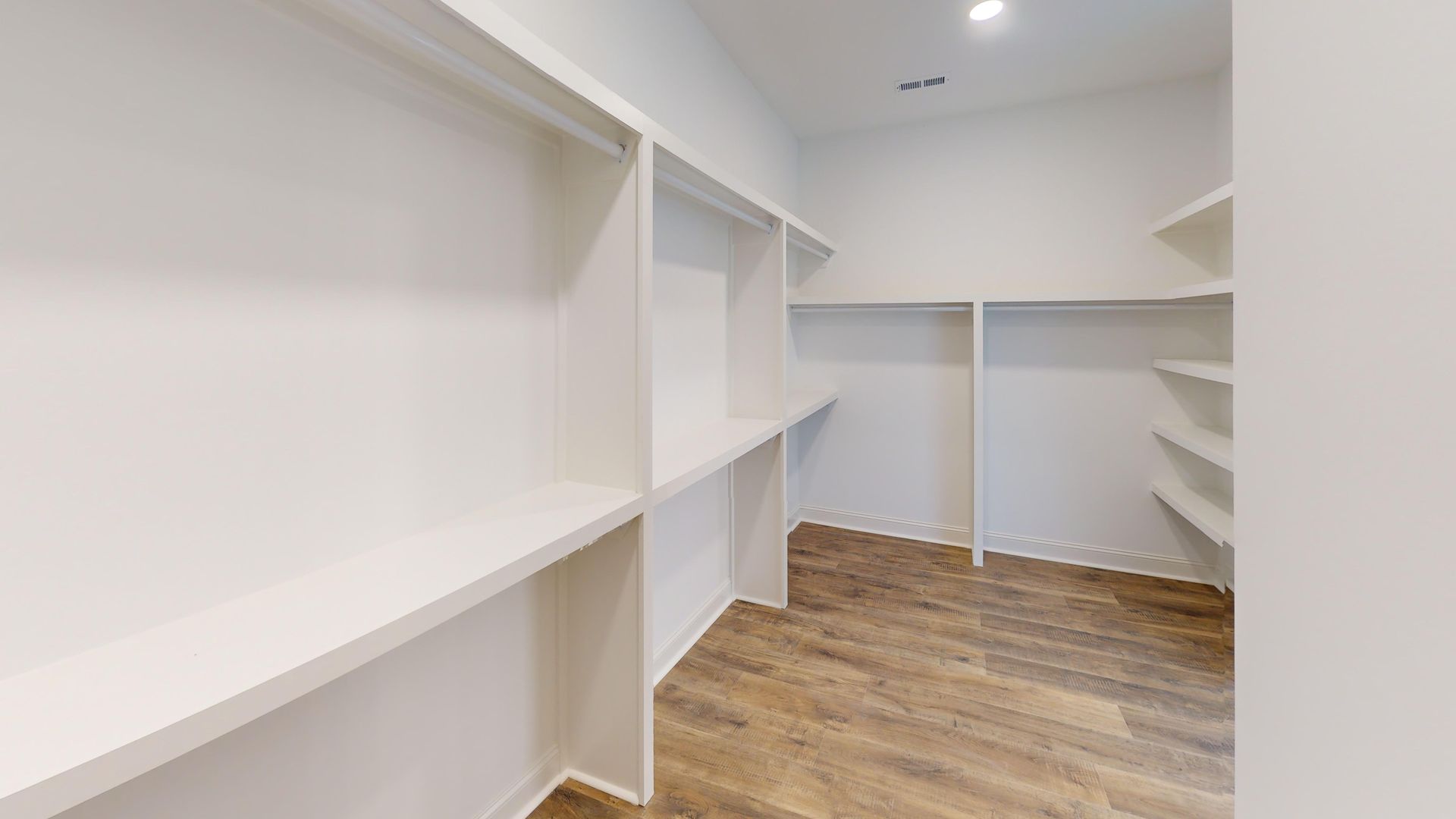 Empty white closet with built-in shelving and wooden floor.