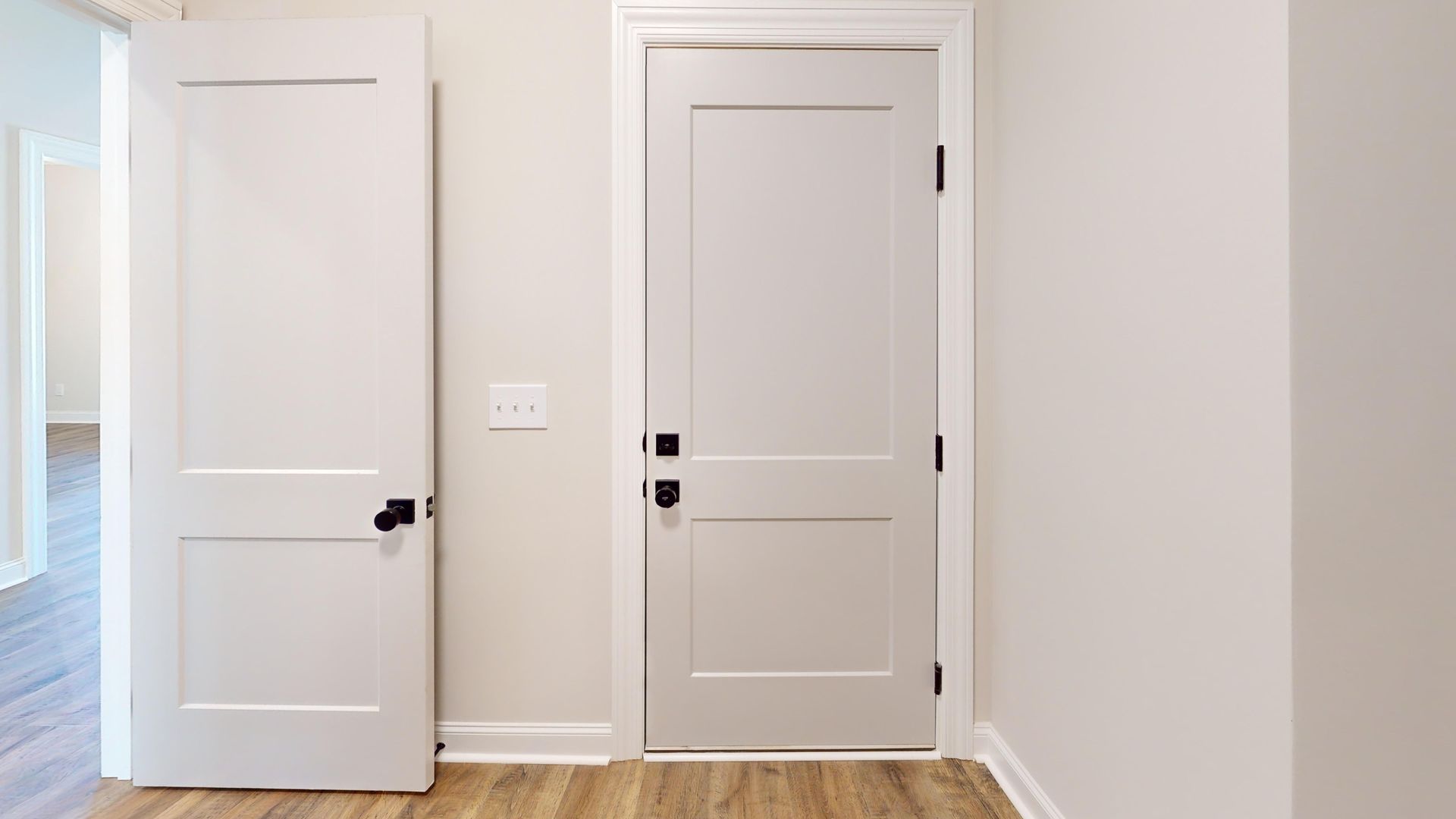 Two white doors in a room with light-colored walls and wood flooring; one door is open.