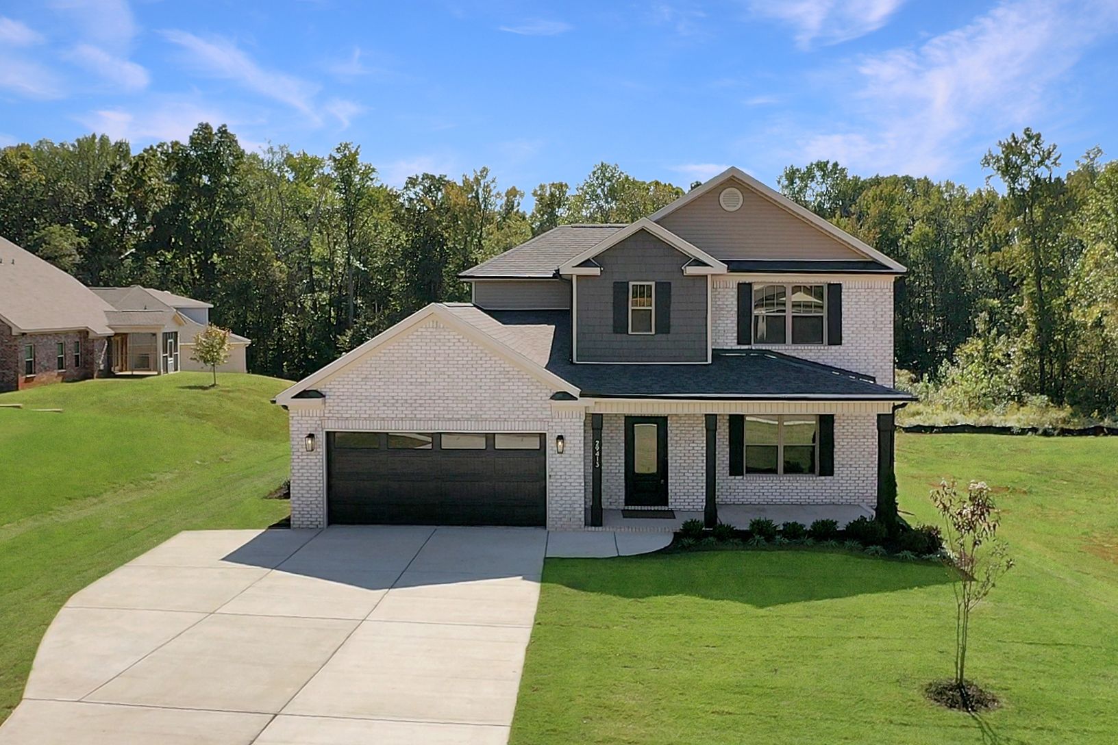 Two-story house with a brick exterior, attached garage, and a green lawn under a blue sky.