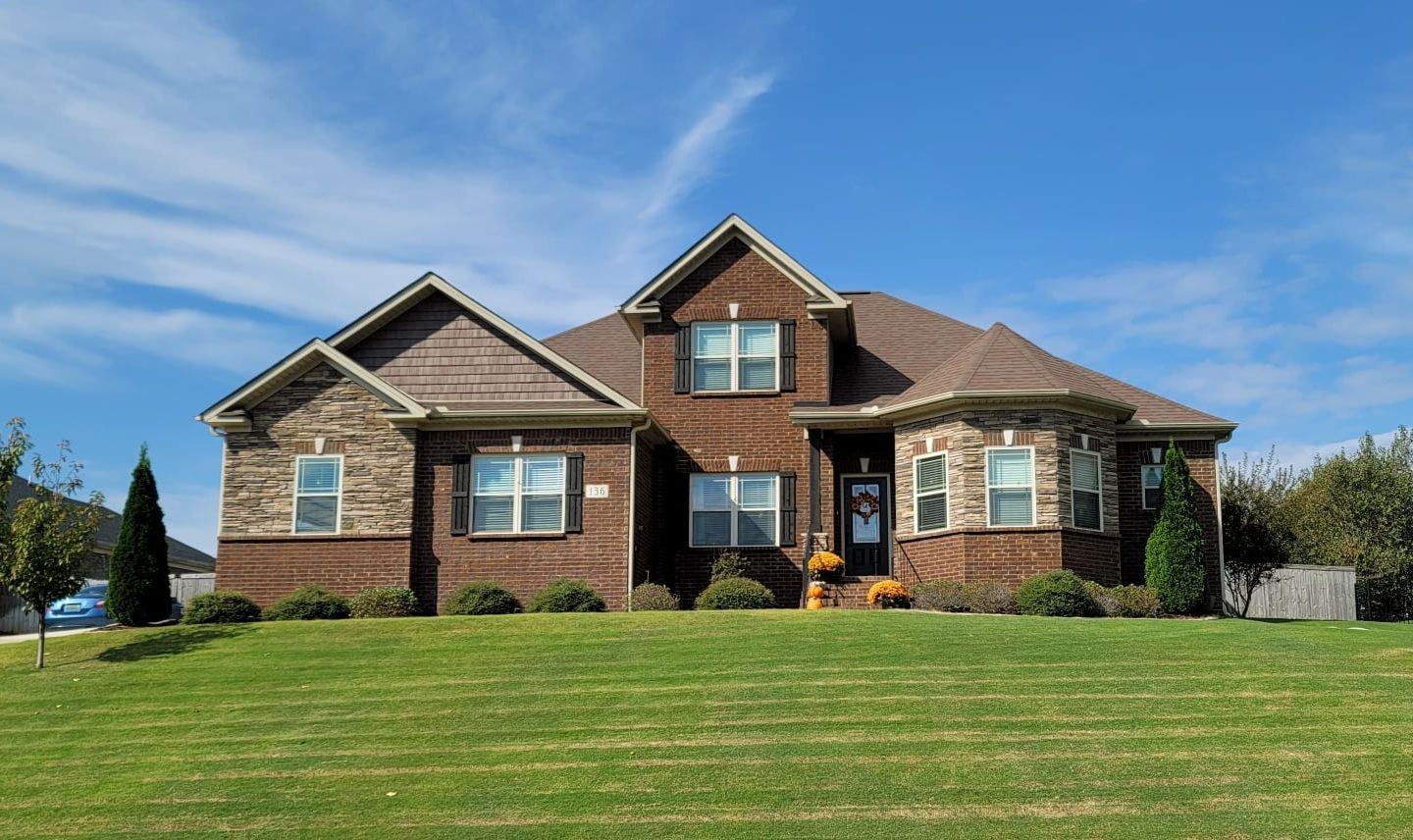 Brick house with brown roof, green lawn, blue sky.