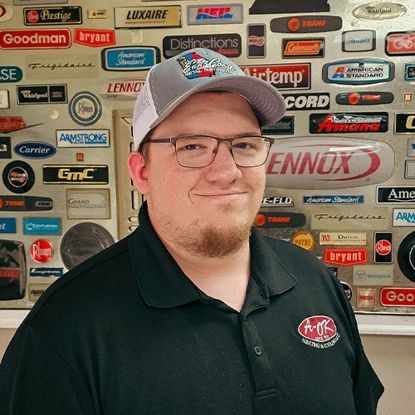 A person wearing glasses and a ball cap stands in front of a wall covered in various HVAC company logos.