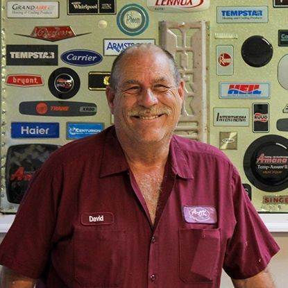A smiling person in a maroon work shirt stands in front of a wall covered in HVAC company logos.
